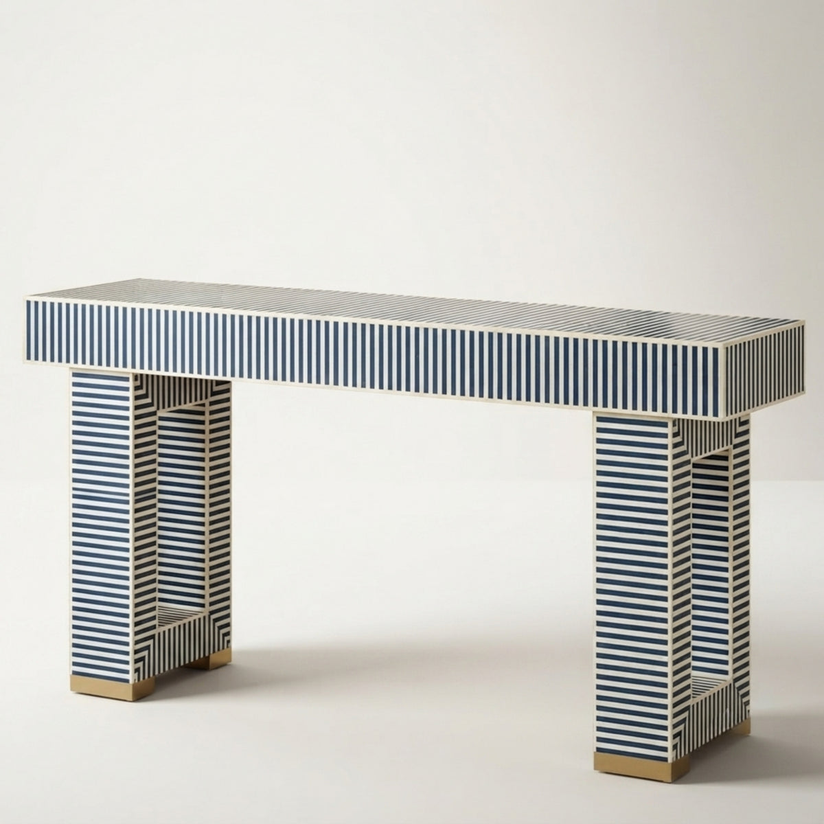 A modern console table with a rectangular top and two legs, both covered in navy blue and beige striped bone inlay, finished with gold-toned metal feet, shown against a plain light gray background.
