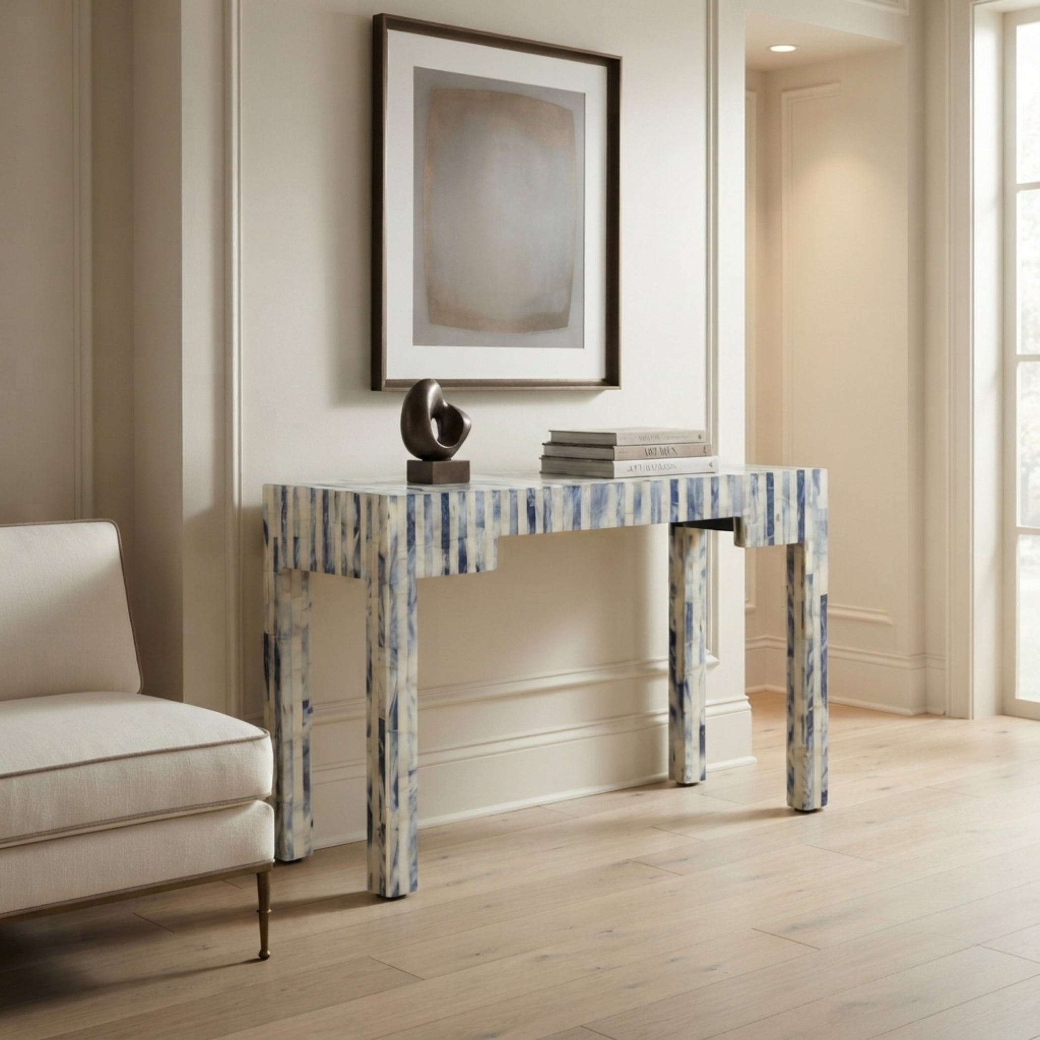 A console table with a blue and white marbled pattern, styled in a bright, modern living room next to a white armchair and beneath a framed abstract print.