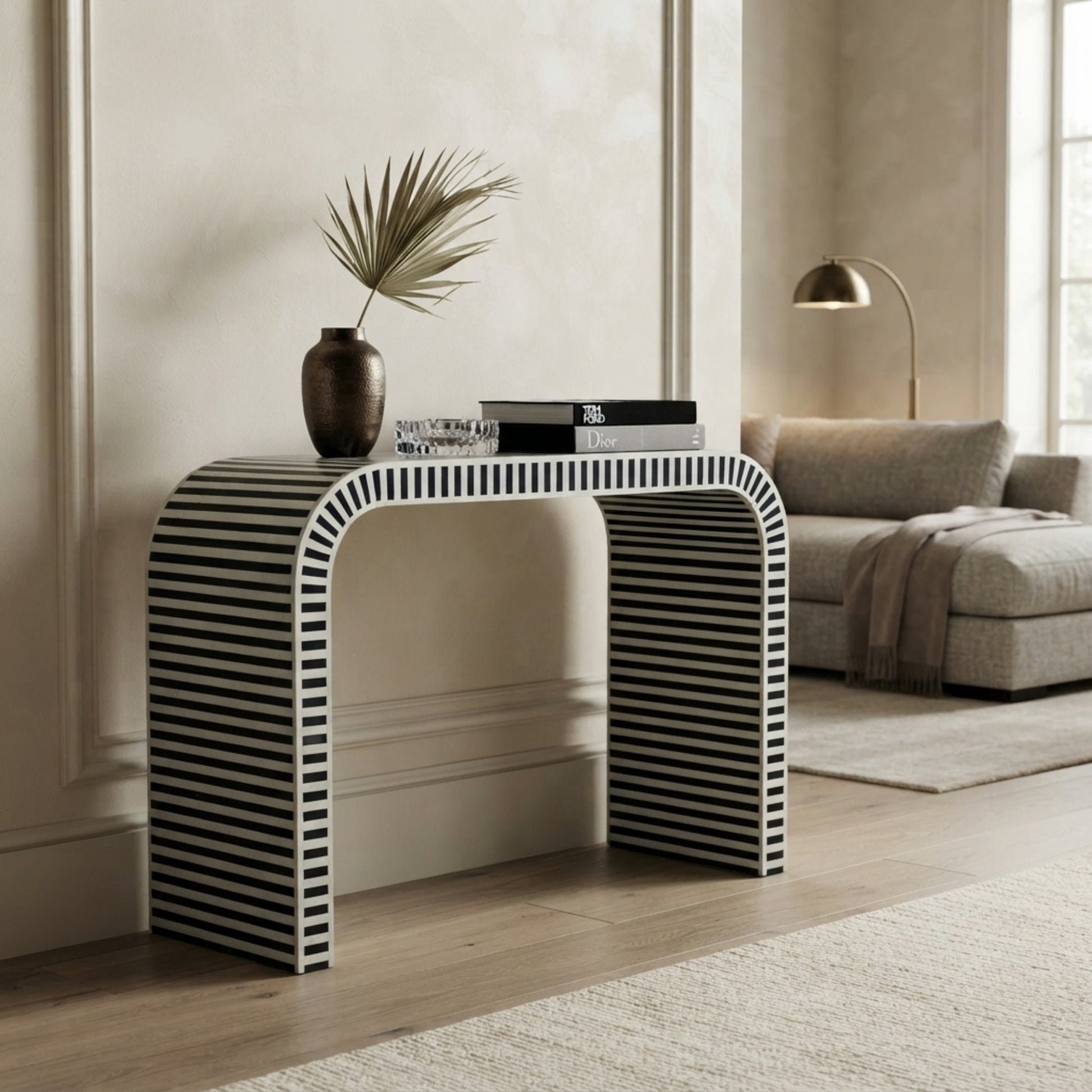A modern console table with a bold black and white striped pattern, styled in a minimalist living room setting with a vase and books on top.
