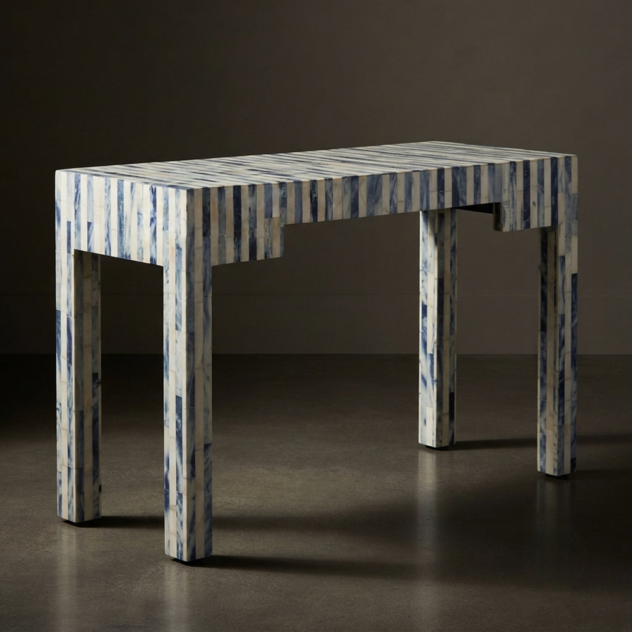 A rectangular table with a blue and white striped bone-in-shell finish, set against a dark brown studio background.