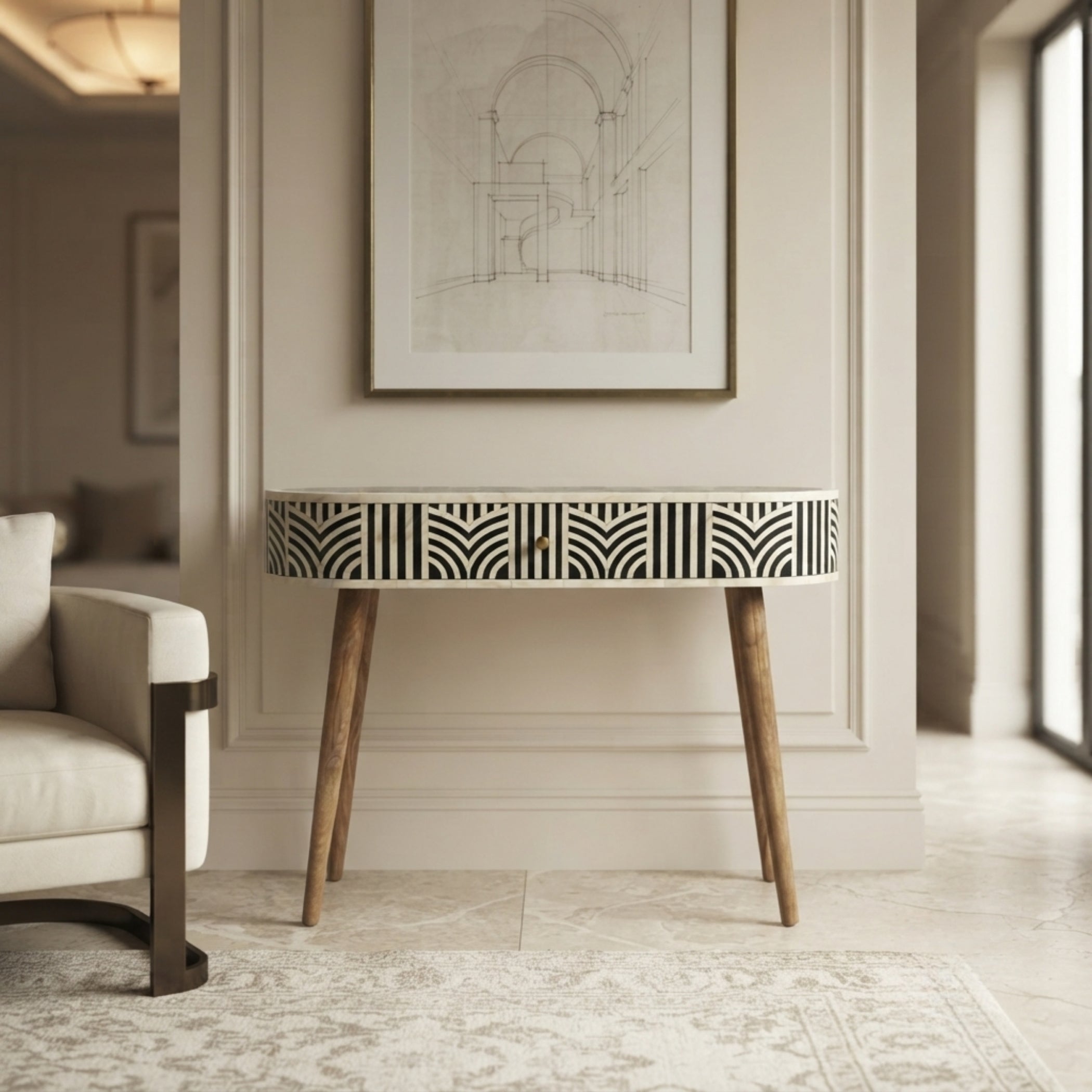 A modern console table with a black and white geometric patterned front and natural wood legs, styled in a bright, elegant room next to a white armchair.