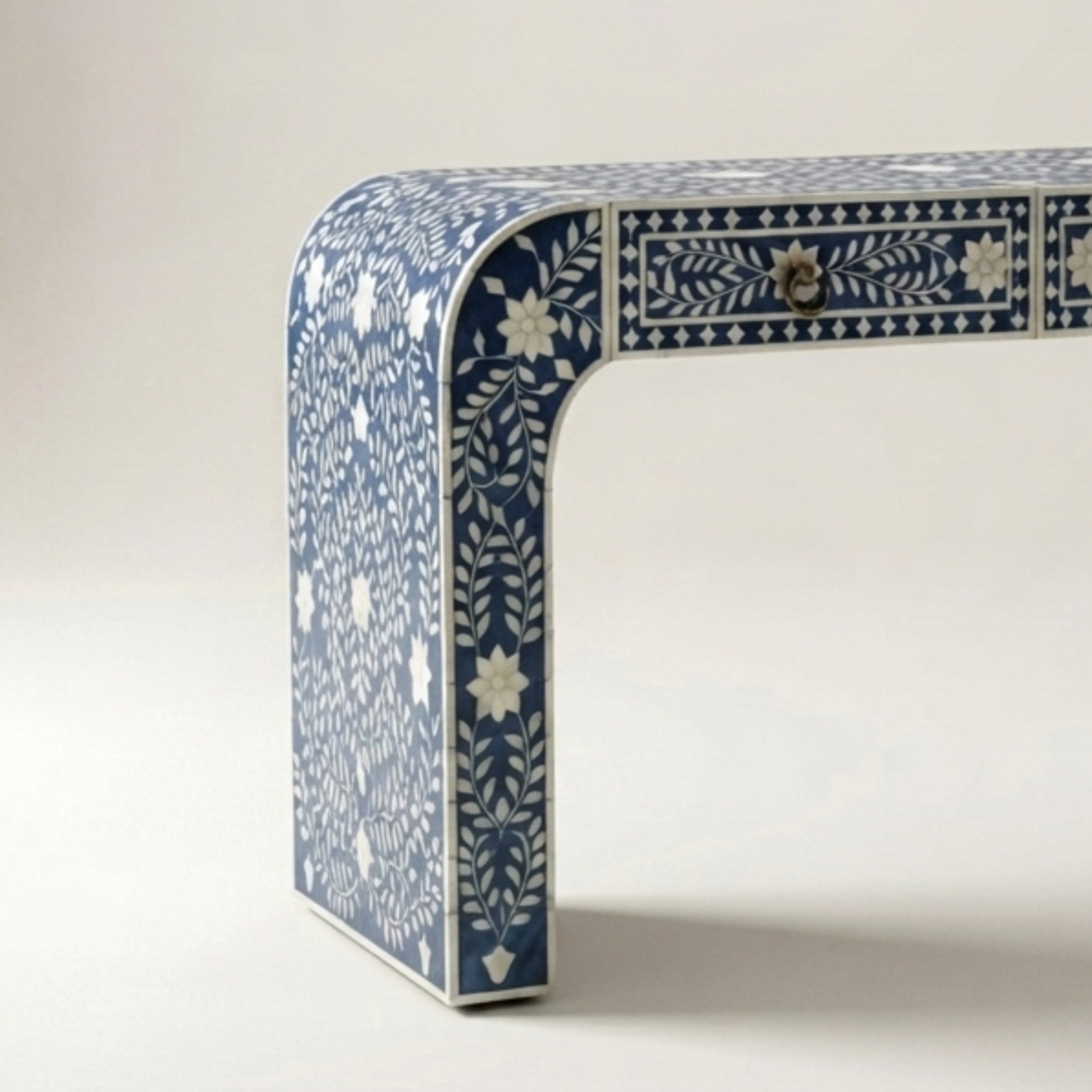 A close-up studio shot of a decorative table leg with a blue and white floral inlay pattern, set against a plain light background.