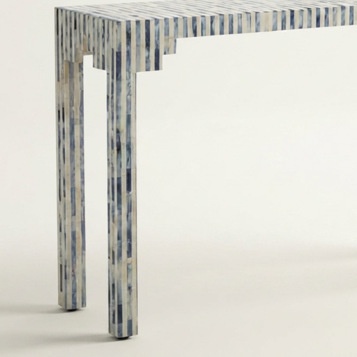 A modern rectangular table with a top and legs featuring a vertical inlay pattern of blue, gray, and white wood or bone-like strips, shown against a plain off-white background.