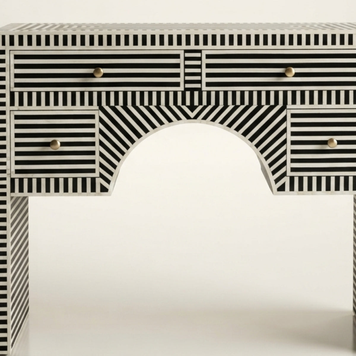 A black and white striped console table with an arched center panel and small round gold drawer knobs, shown against a plain white background.