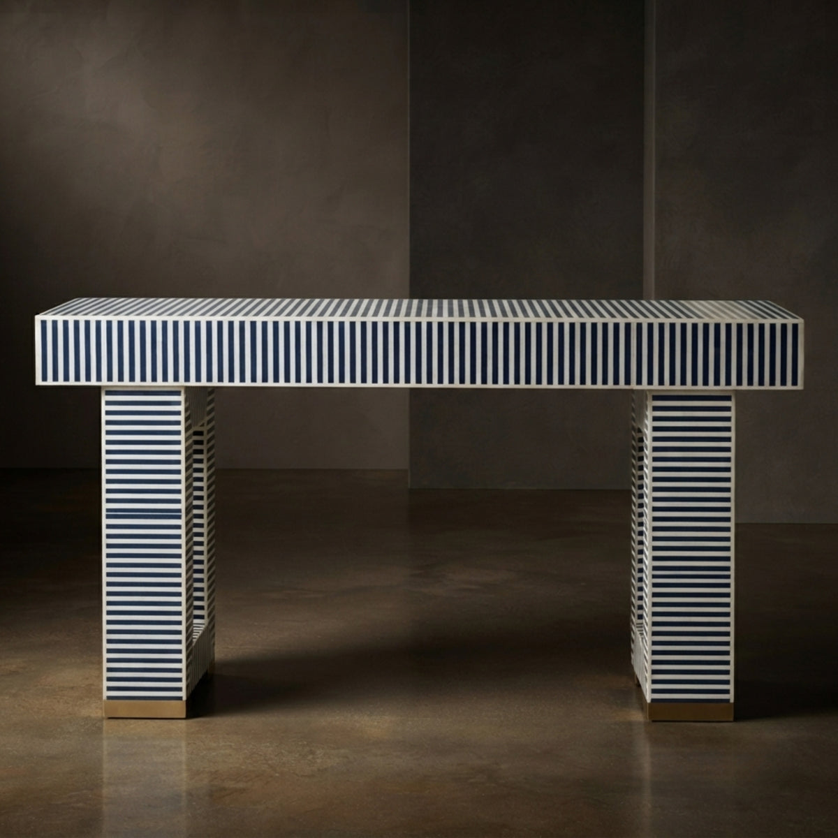 A modern rectangular console table with a white top and legs featuring vertical navy blue and white stripes, finished with small gold metal feet, set against a dark textured studio background.