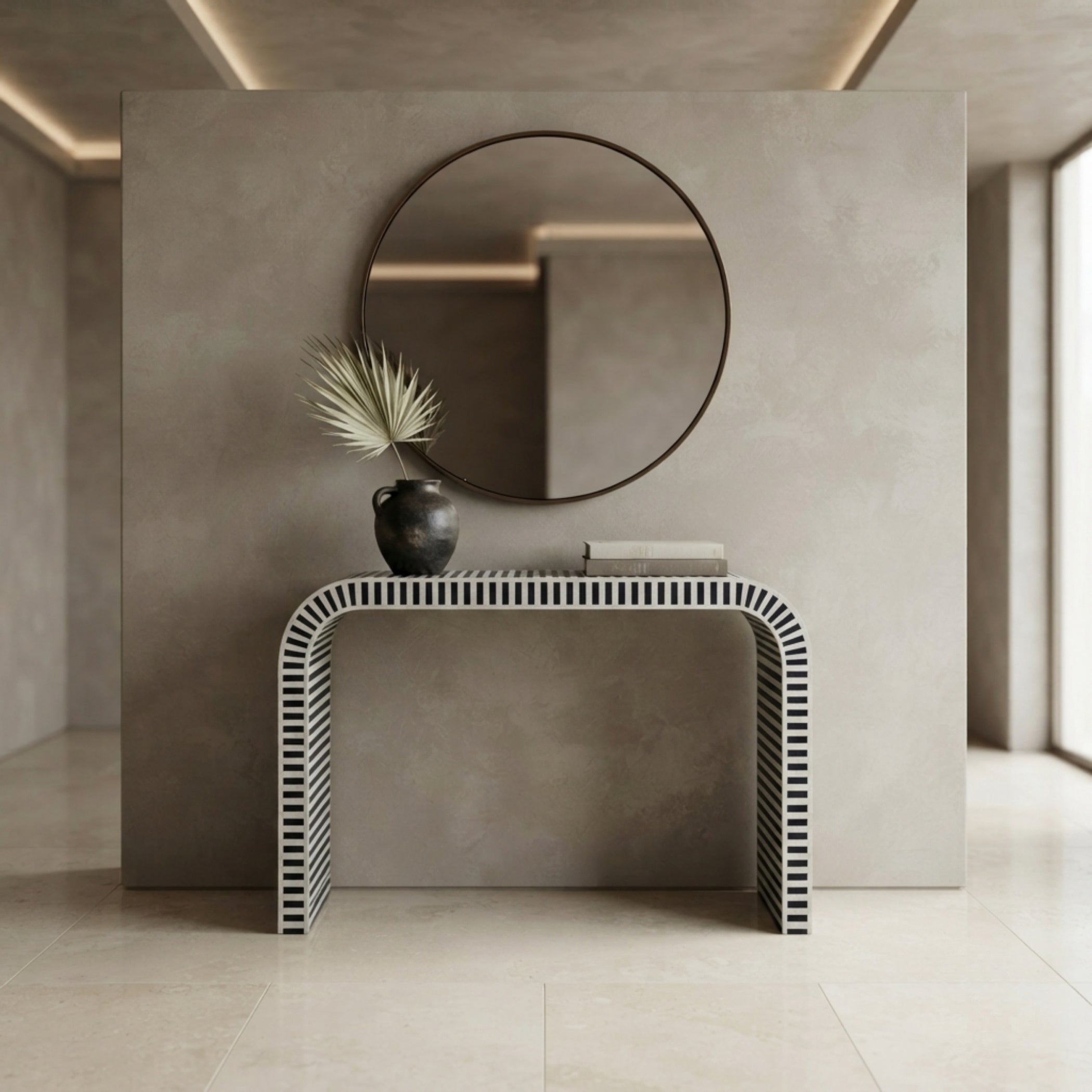 A modern console table with a black-and-white vertically striped wavy frame, styled in a minimalist entryway with a round wall mirror, a small vase with dried leaves, and a book.