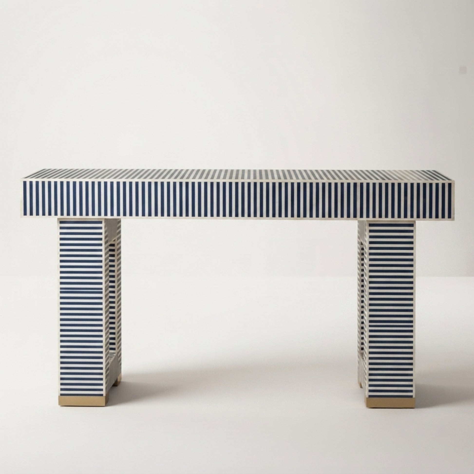 A modern console table with a rectangular top and two matching legs, both covered in navy and white horizontal stripes, with small gold-toned metal feet at the bottom, set against a plain light gray background.