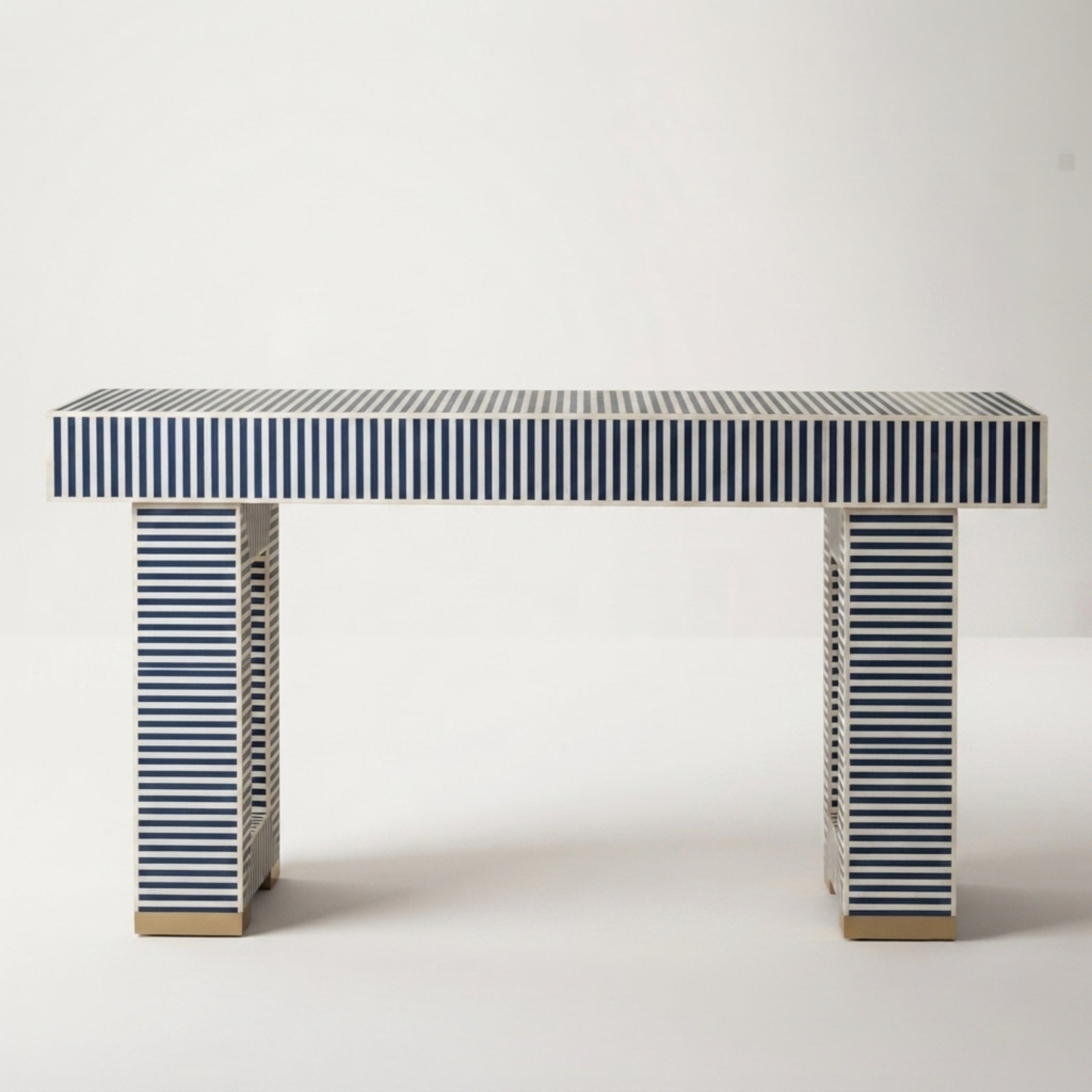 A modern console table with a rectangular top and two matching legs, both covered in navy and white horizontal stripes, with small gold-toned metal feet at the bottom, set against a plain light gray background.