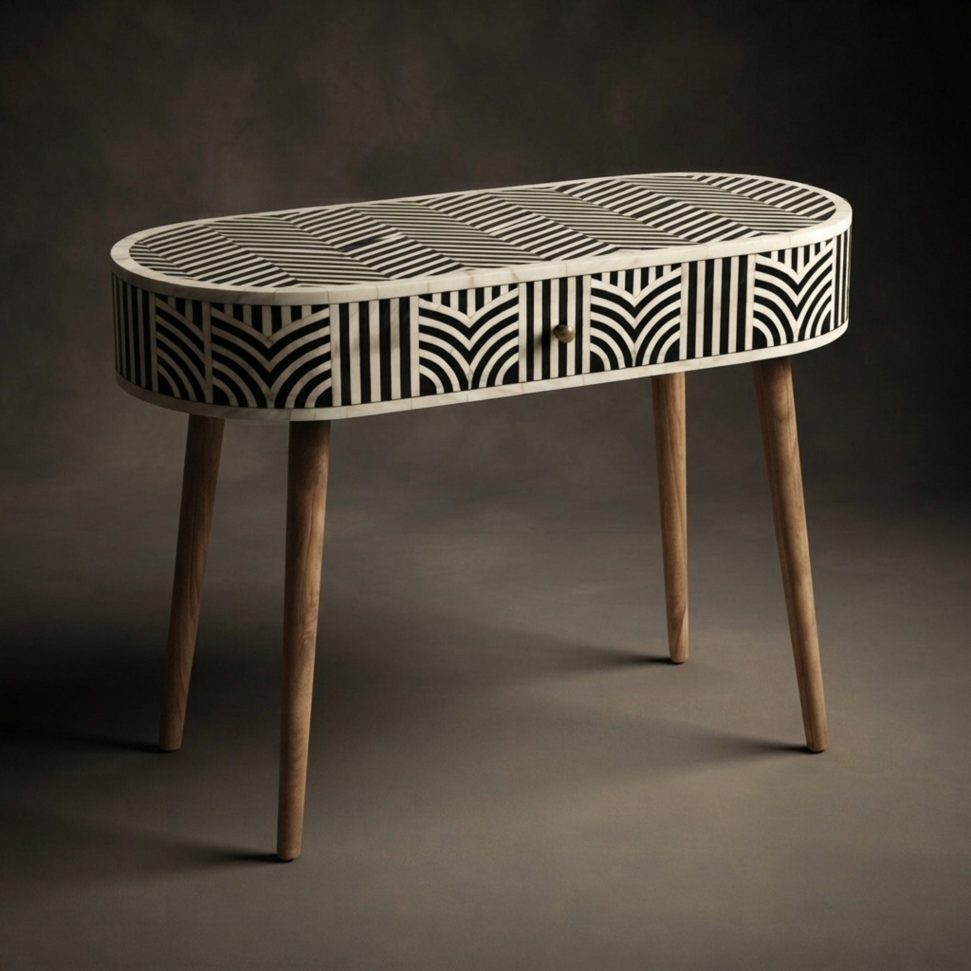 An oval console table with a black and white geometric bone-inlay pattern on the top and sides, supported by four tapered natural wood legs, set against a dark gray studio background.