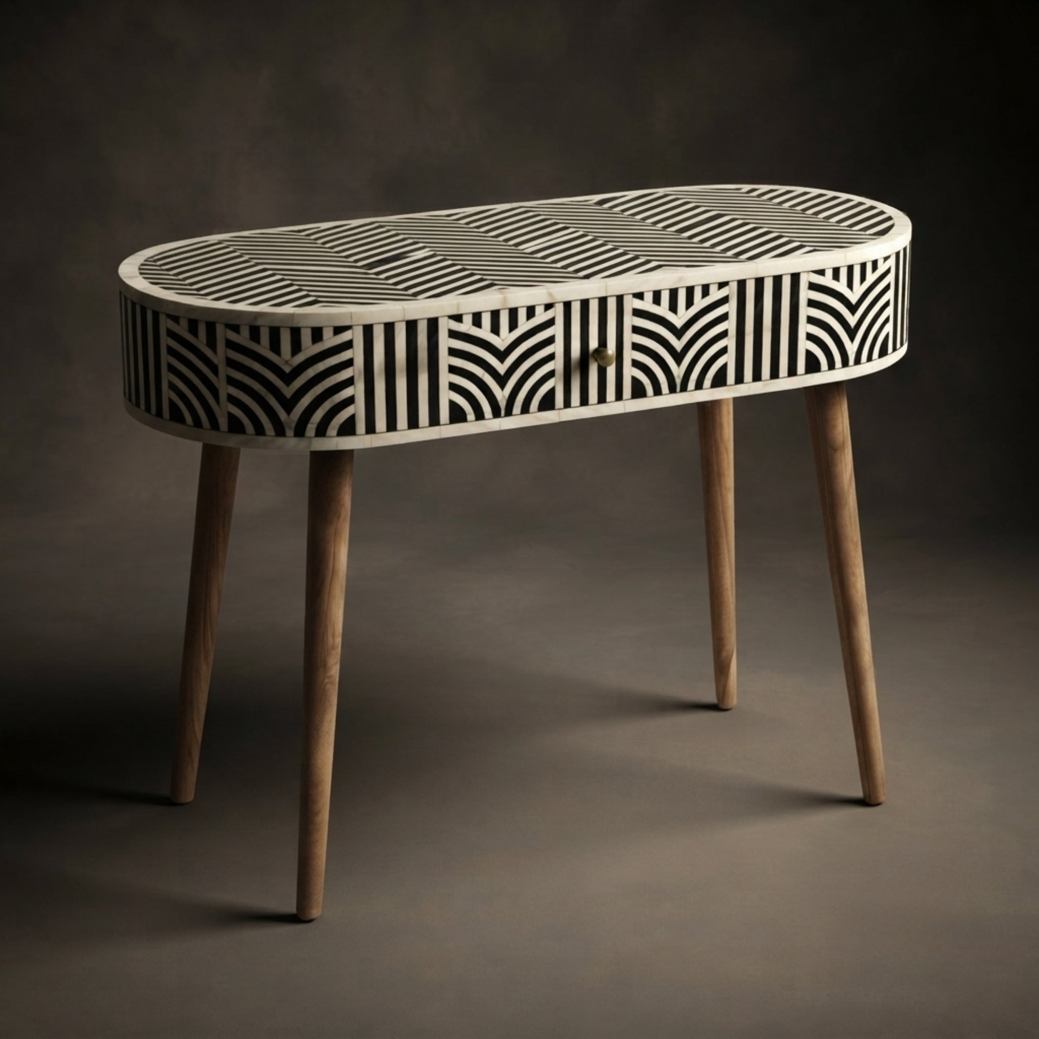 An oval console table with a black and white geometric bone-inlay pattern on the top and sides, supported by four tapered natural wood legs, set against a dark gray studio background.