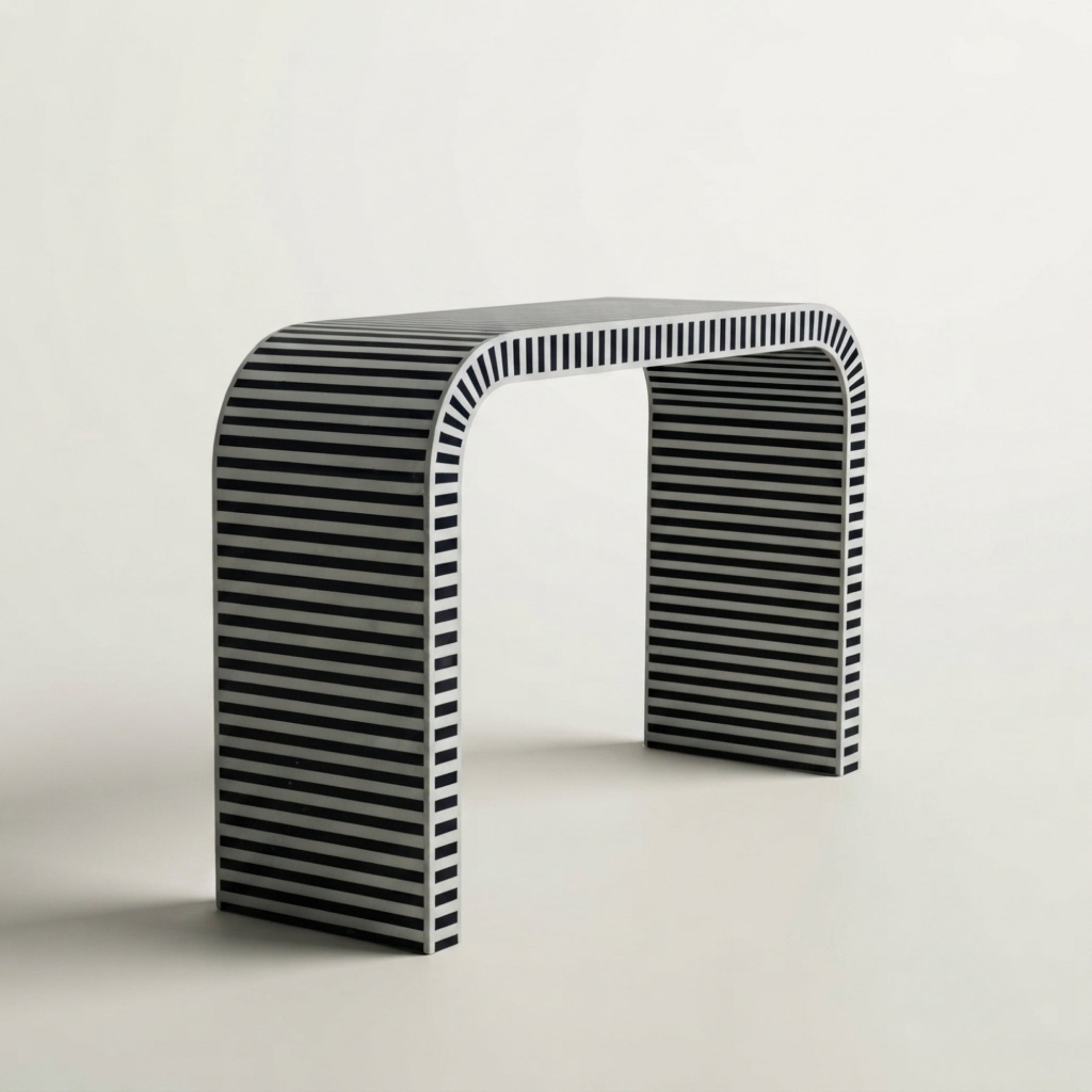 A modern minimalist console table with a curved top and legs, featuring a black and white horizontal striped pattern, set against a clean off-white background.