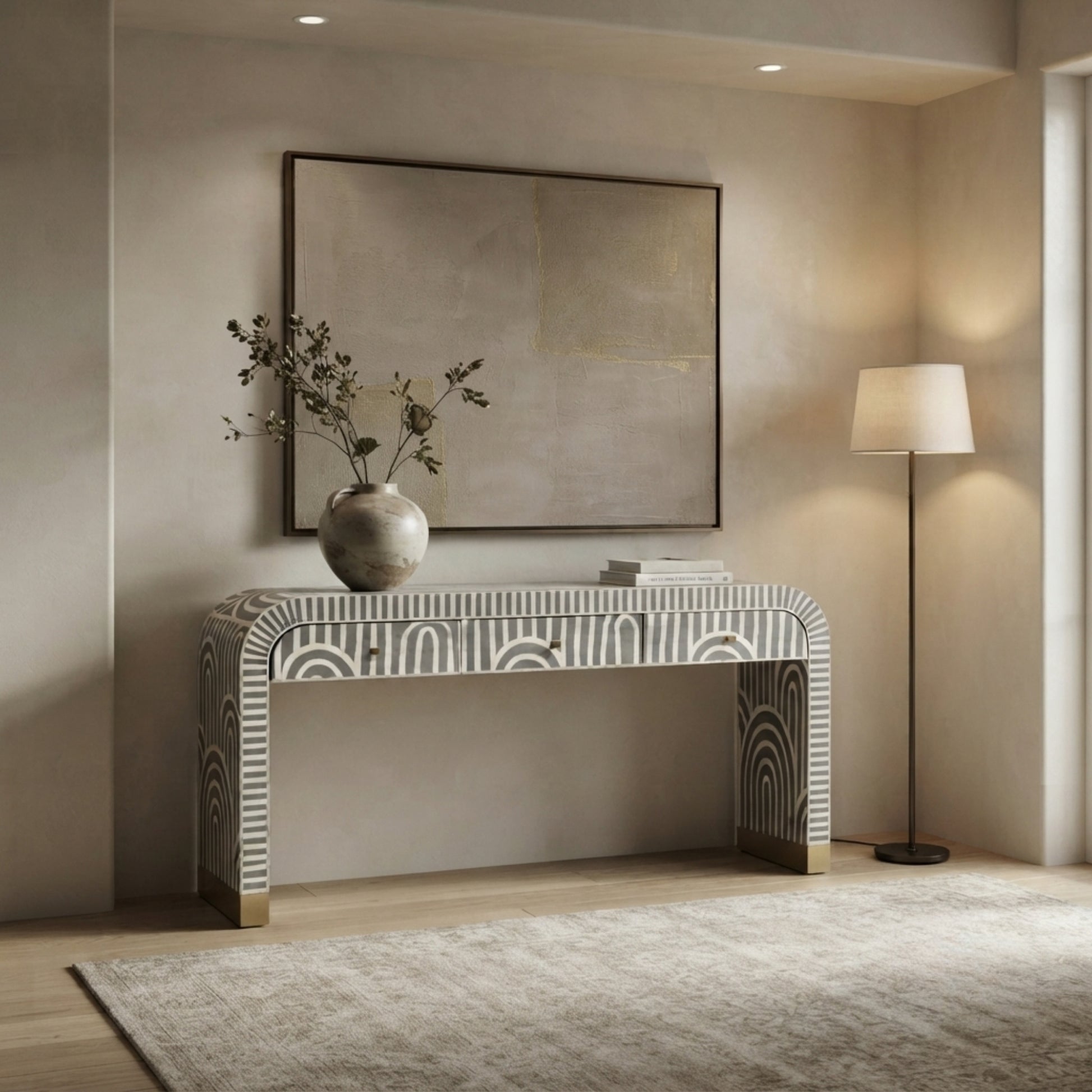 A modern console table with a white and gray geometric patterned bone-inlay frame, styled in a warm, minimalist entryway with a large abstract painting, a floor lamp, and a vase of branches.
