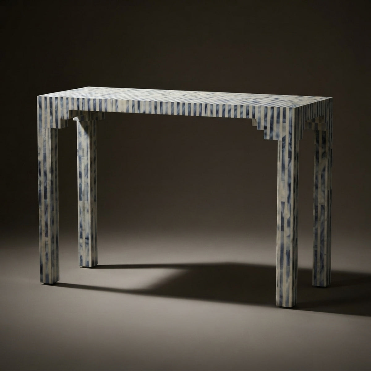 A rectangular console table with a blue and white striped bone-look finish, set against a dark brown studio background.