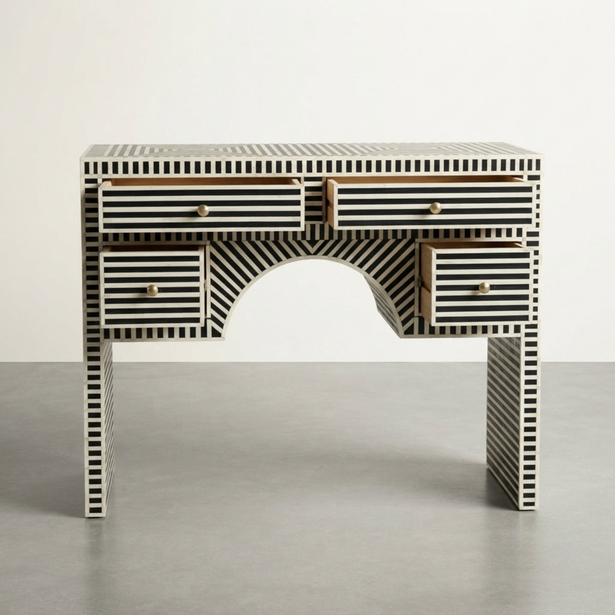 A bone-and-ivory desk with black and white striped patterns, featuring five drawers and a central arched opening, set against a neutral studio background.