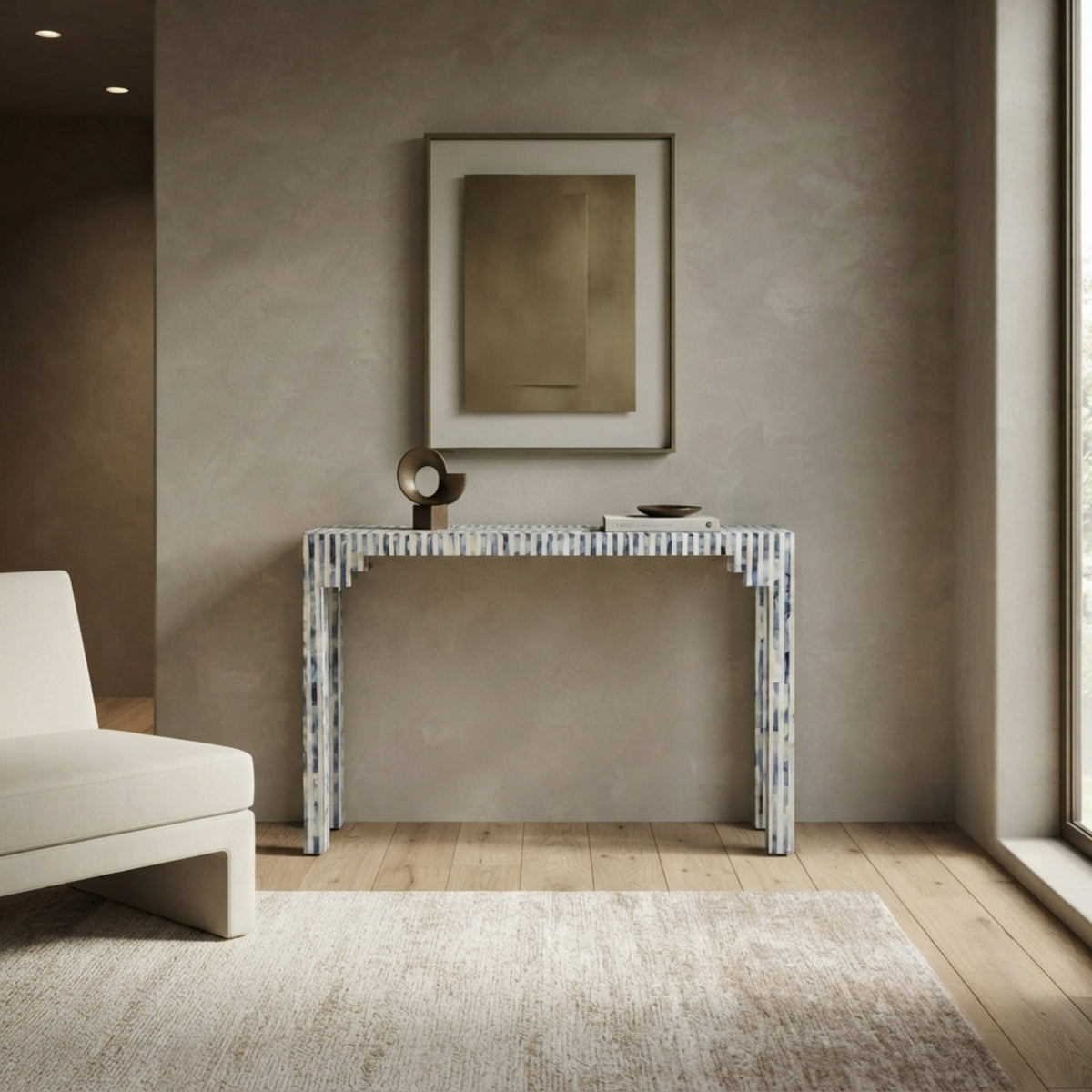 A modern console table with a blue and white striped shell-like frame, styled in a minimalist living room with a textured beige wall, light wood floor, and a white sofa partially visible on the left.