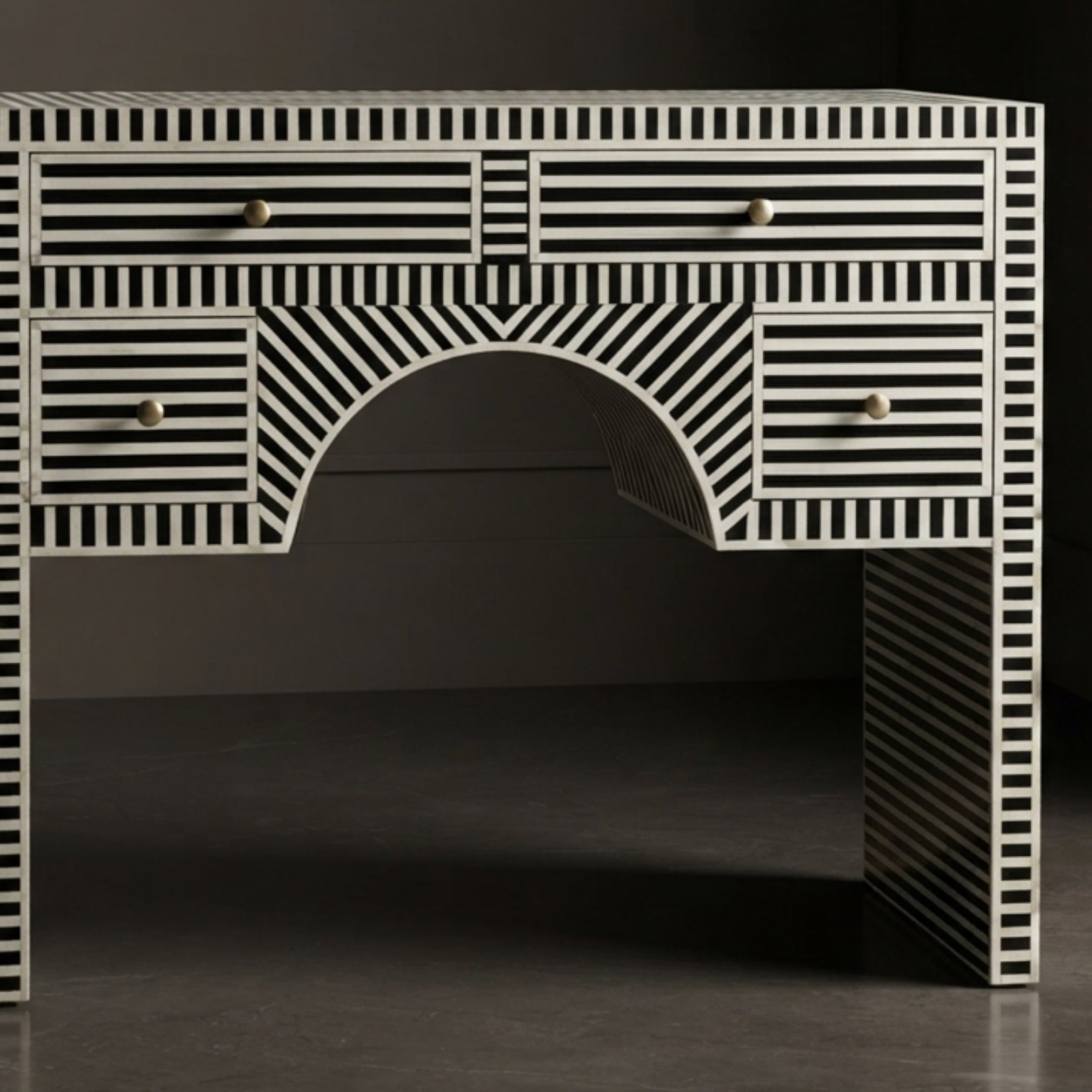 A black and white striped bone-inlay writing desk with an arched center and small round gold knobs, shown against a dark studio background.