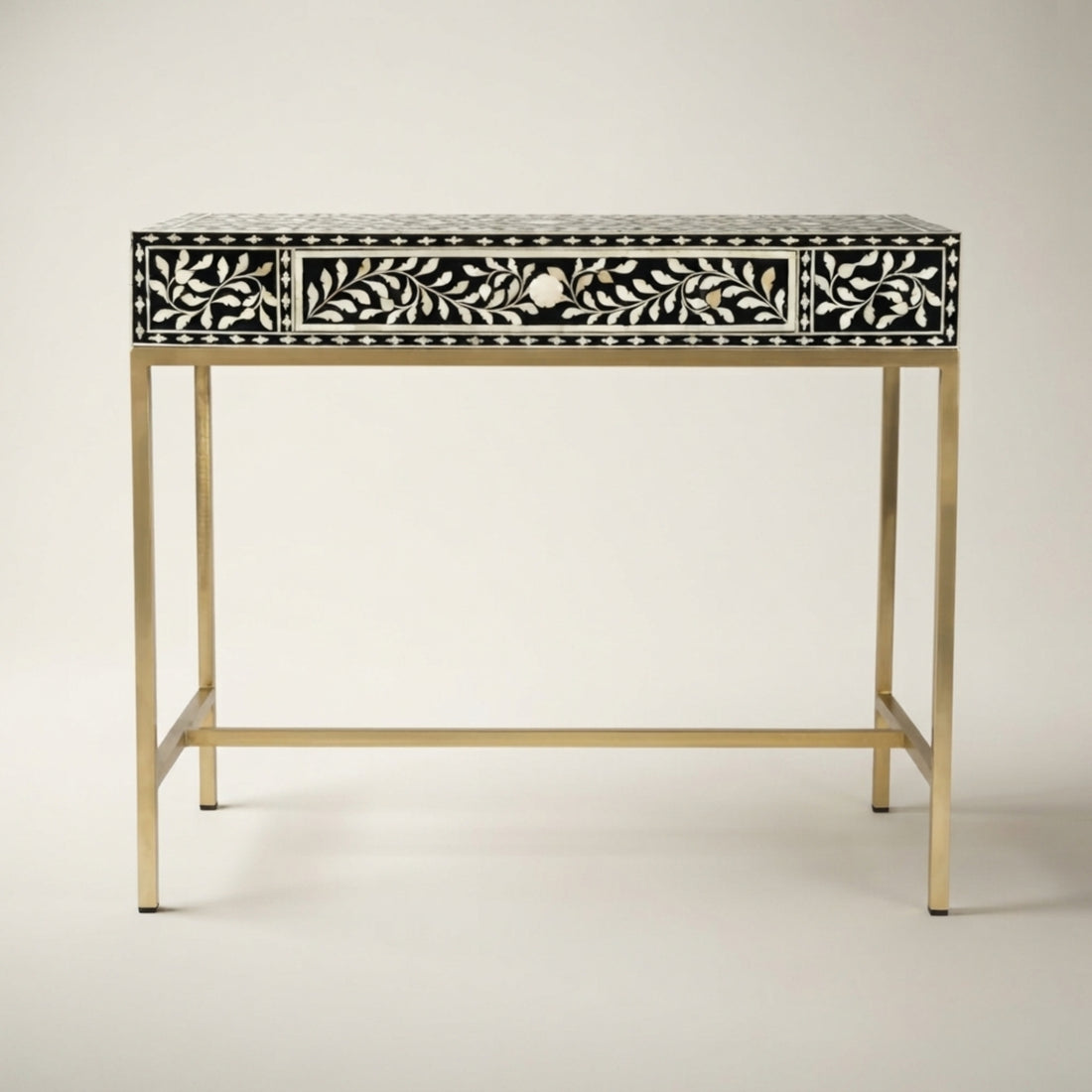An ornate console table in a luxurious room setting, featuring a black and gold Art Deco patterned bone-inlay drawer front, gold metal legs, and a single open drawer. The table is styled with two black table lamps, a deer sculpture, and a sunburst mirror on a patterned black, gold, and white floor.