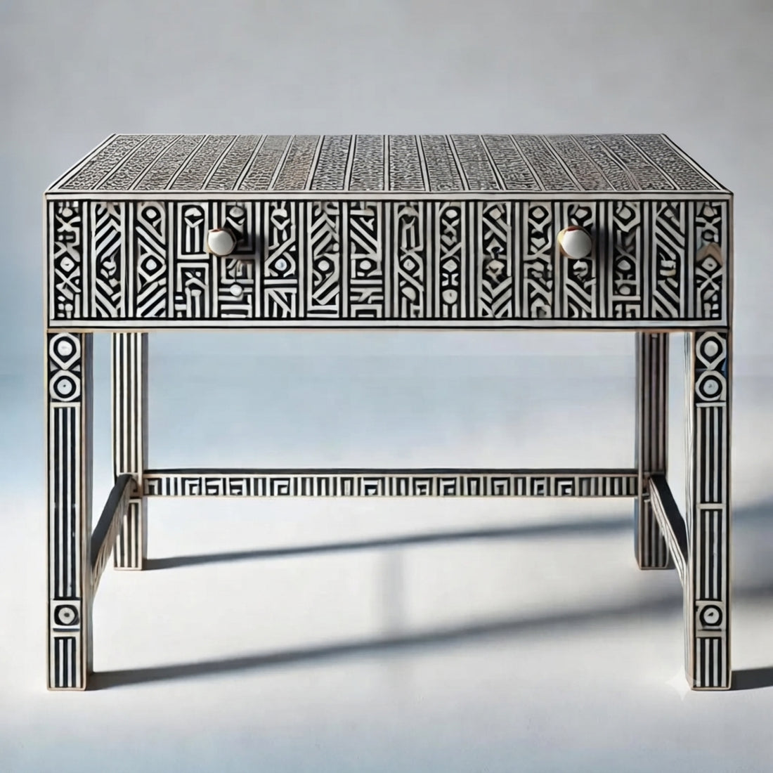 An ornate console table with geometric bone-inlay detailing, styled in a bright, modern room with a round mirror, wall sconces, and a vase of palm leaves.