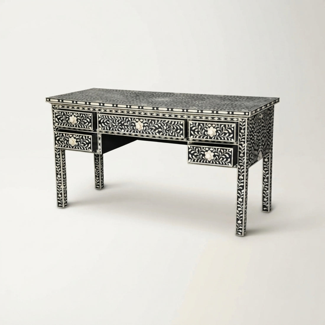 A black and white bone-inlay writing desk styled in a warm, neutral-toned room next to a cream upholstered chair, with a table lamp on top.