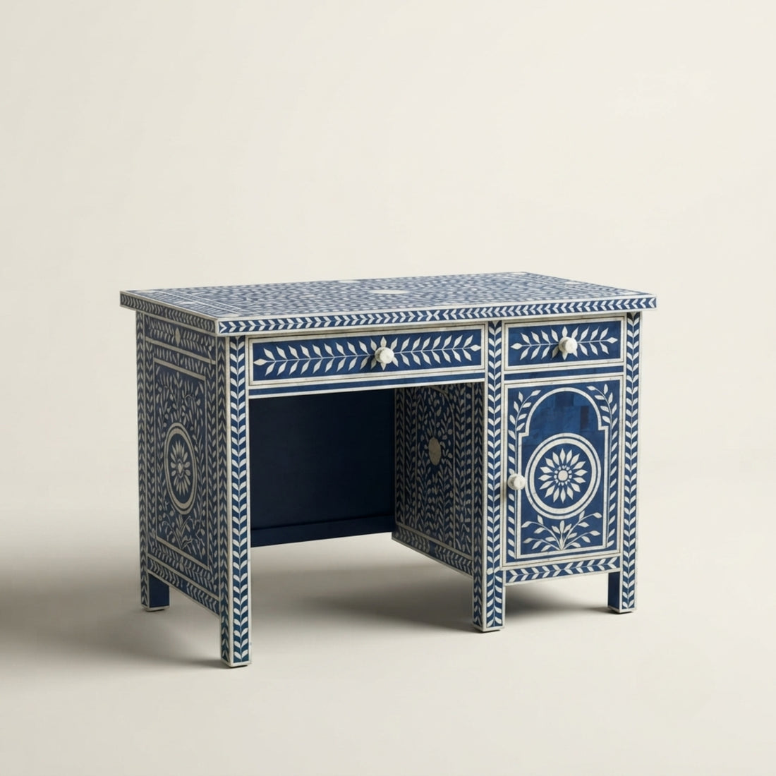 A navy blue and white bohemian-style wooden writing desk with intricate bone-inlay patterns, shown in a decorated room setting with a patterned rug, plants, and wall art.