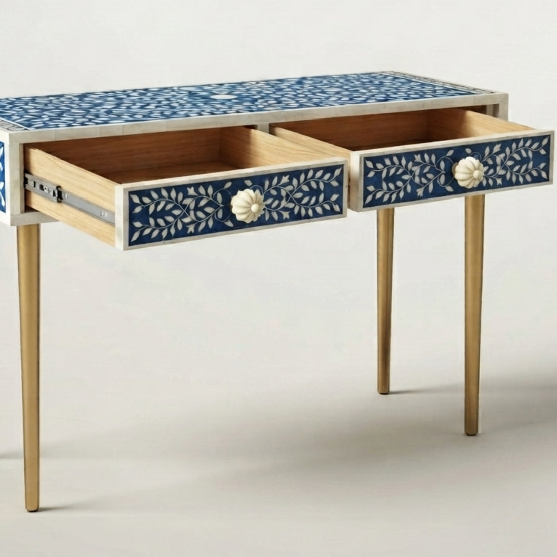 A decorative console table with two blue and white patterned drawers and gold legs, styled in a modern entryway with a vase and small box on top.