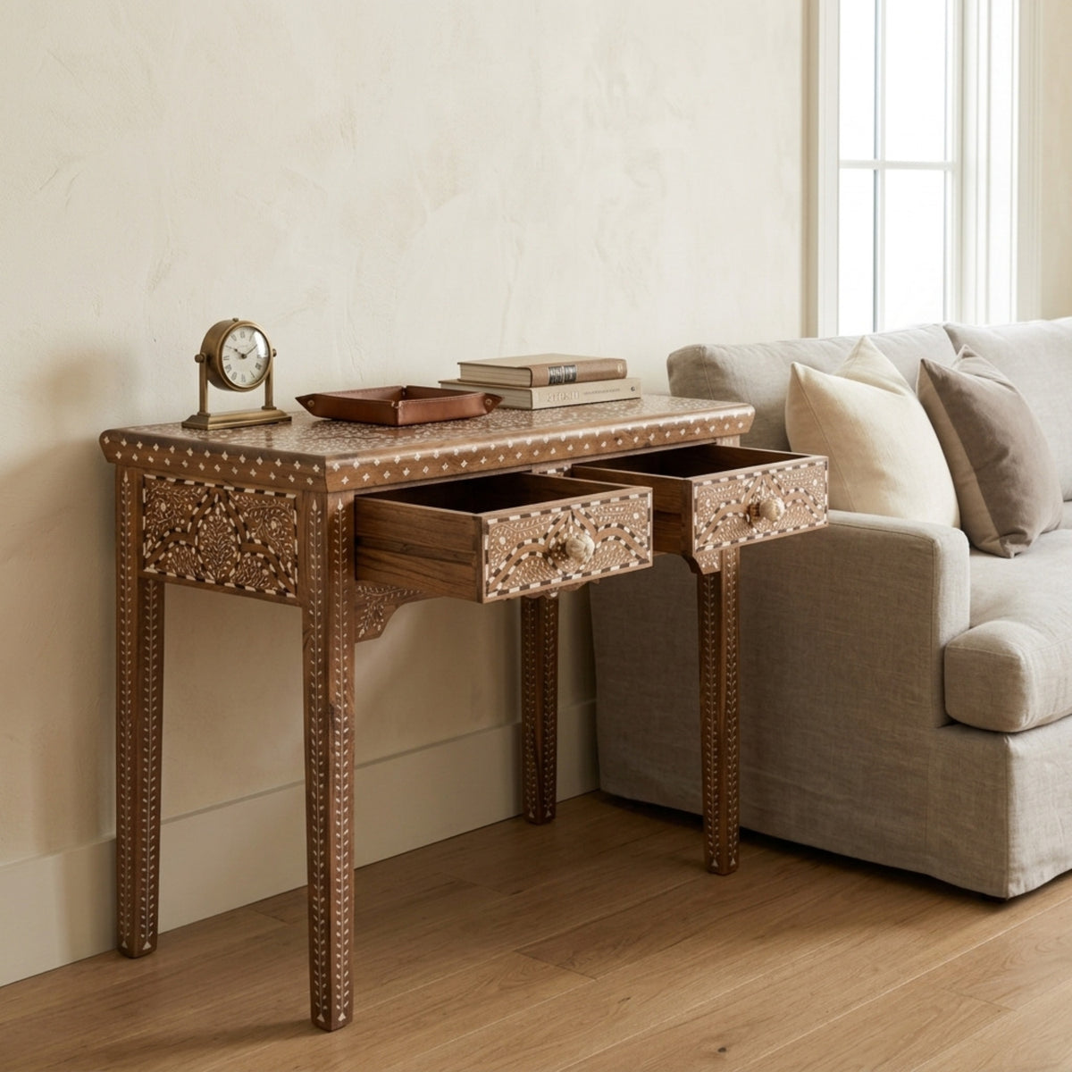 An ornate wooden console table with intricate mother-of-pearl inlay and two open drawers, styled in a living room next to a light gray sofa.