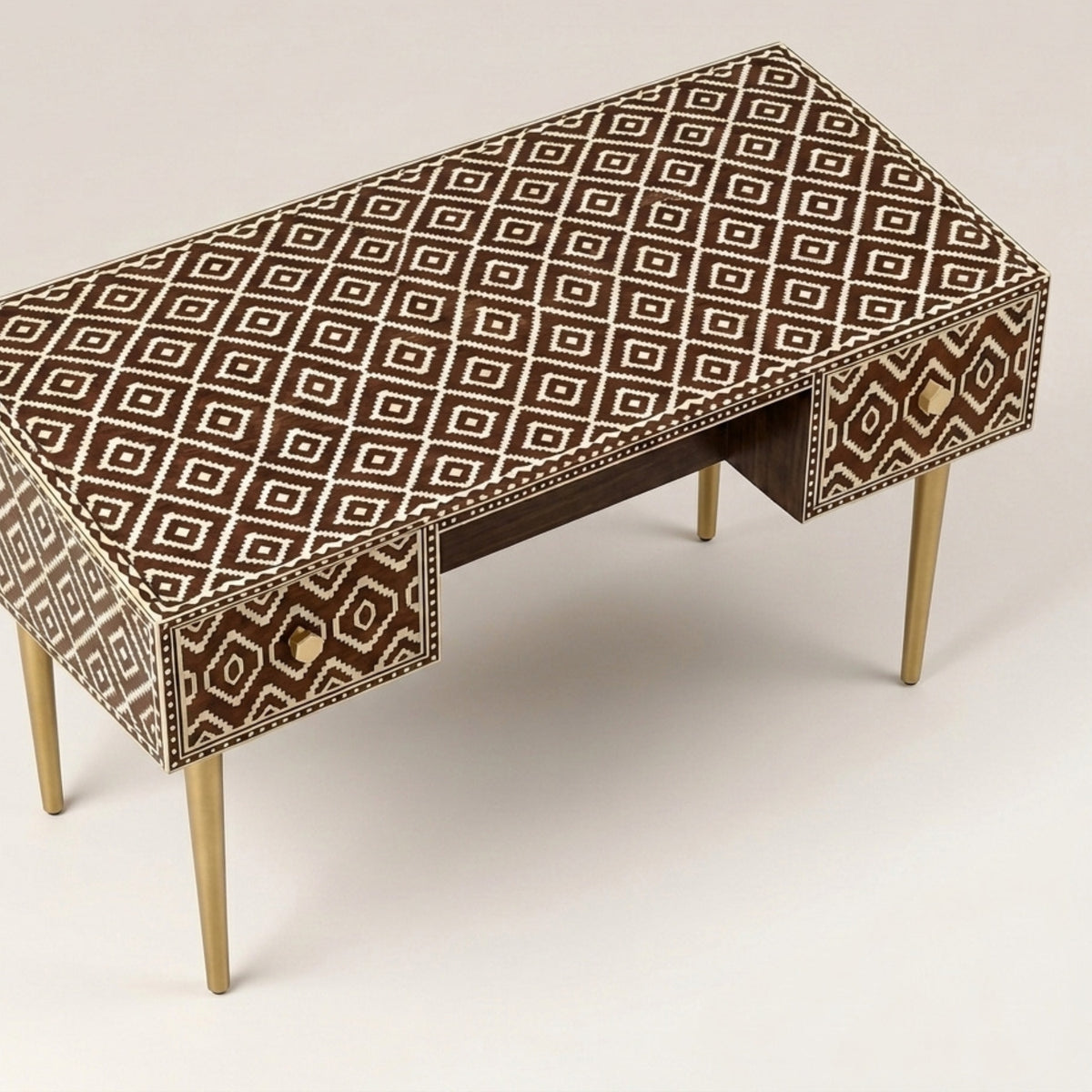 A writing desk with a brown and beige geometric diamond pattern on the top and drawer fronts, supported by four slim gold-toned legs.