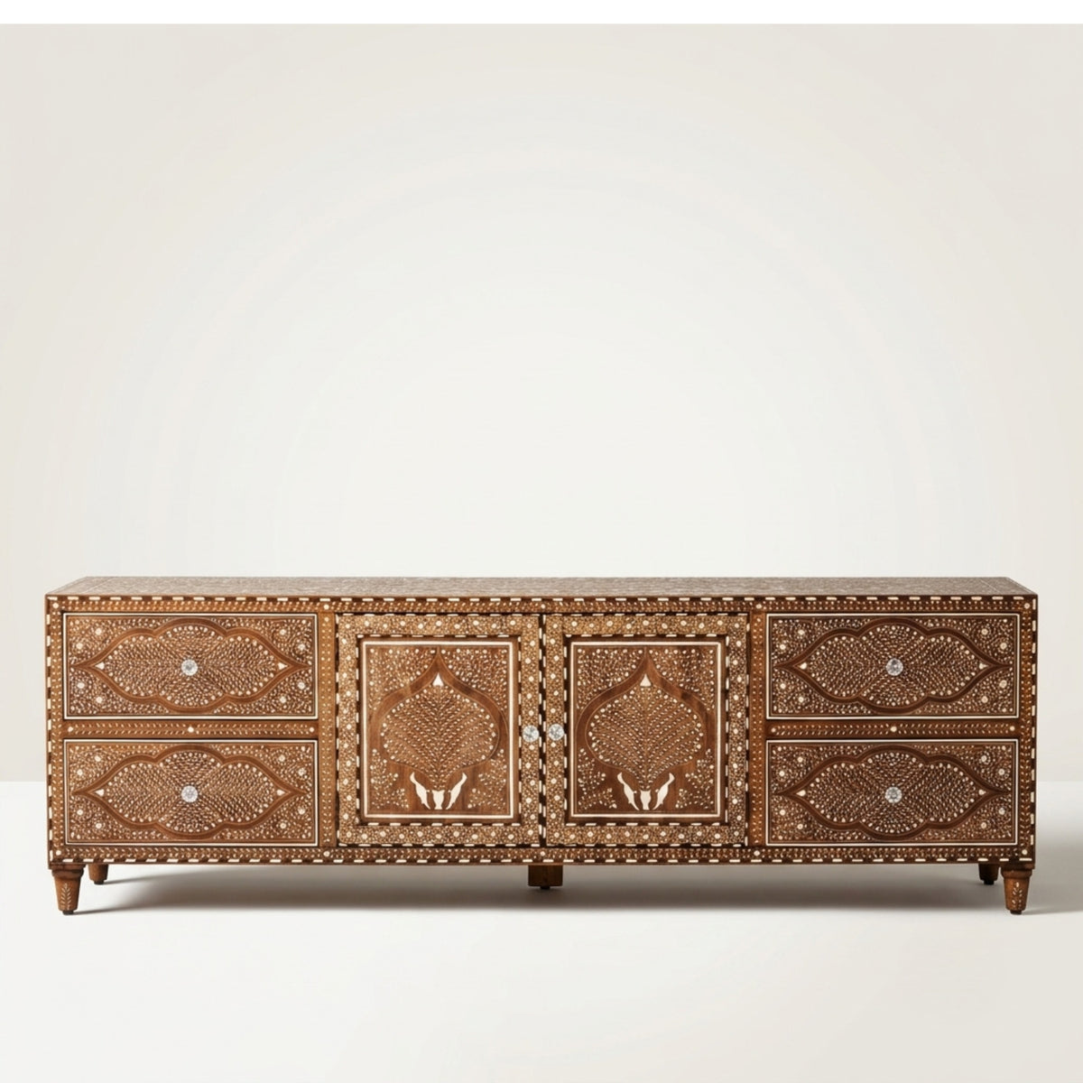 A wide brown wooden sideboard or credenza with ornate carved floral and geometric patterns, small drawers on the sides, and two central doors, photographed against a plain light gray studio background.