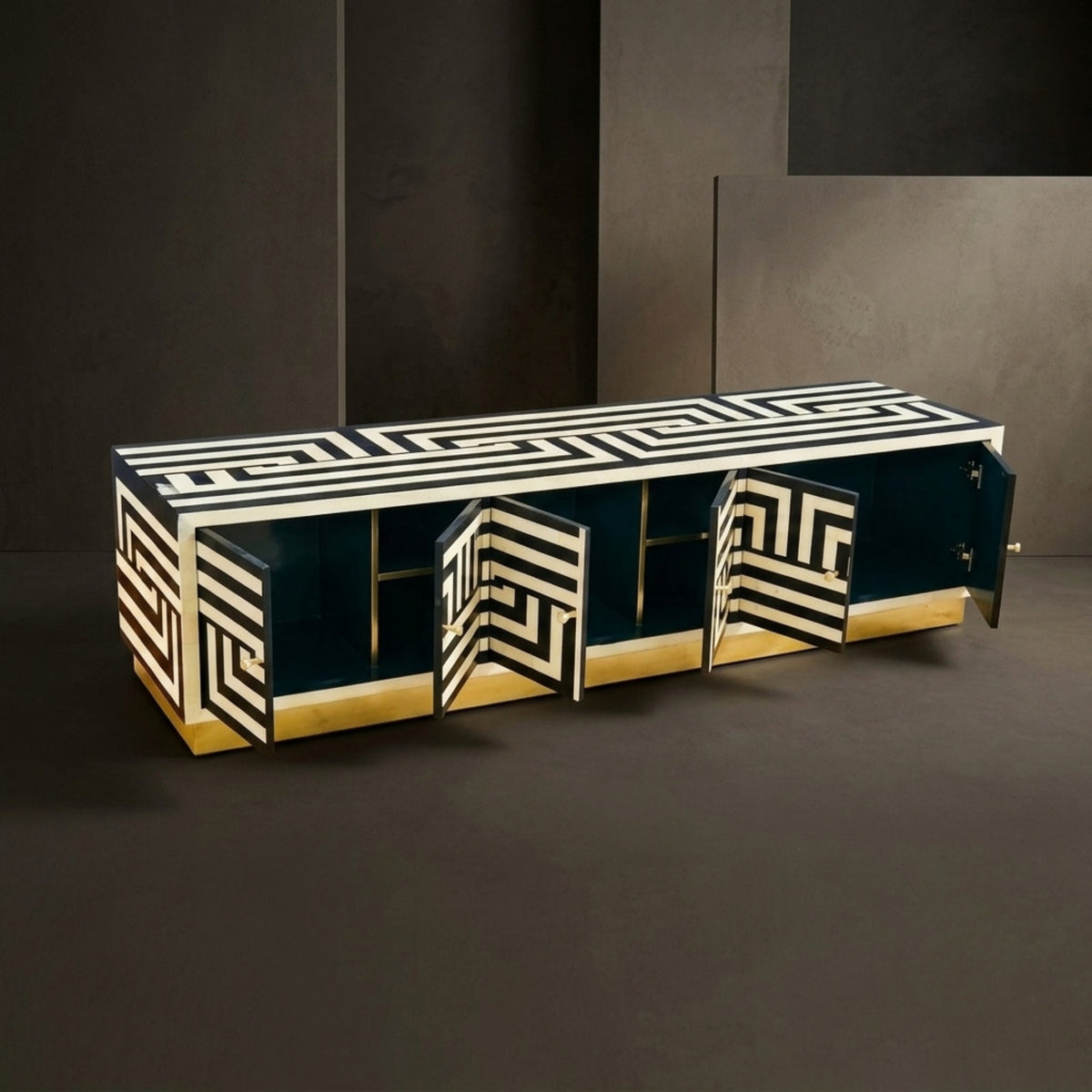 A modern sideboard cabinet with a black and white geometric pattern on the top and doors, dark teal-blue interior panels, and a gold base, shown open against a dark studio background.