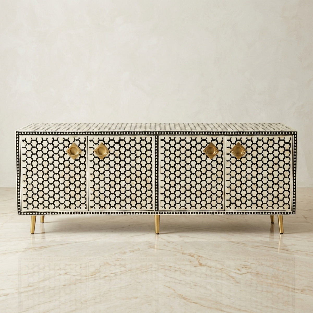 A modern sideboard cabinet with a black and white geometric honeycomb bone-inlay pattern, accented by brass hardware and gold-toned legs, set against a neutral marble background.