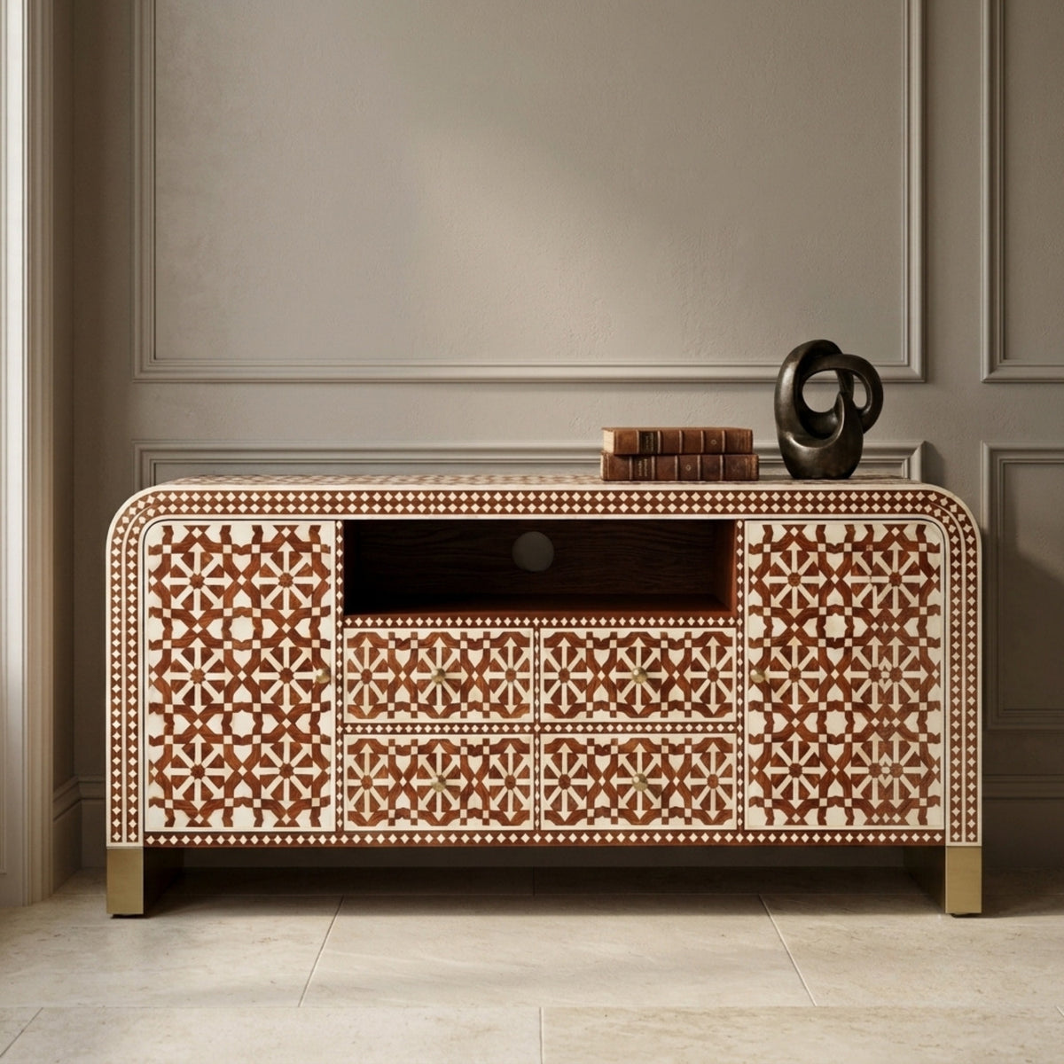 A decorative sideboard cabinet with an intricate brown and beige geometric inlay pattern, featuring three drawers, a central open shelf, and gold-toned legs, styled in a classic interior setting.