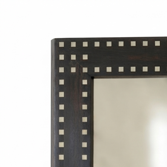 Close-up of a rectangular wall mirror with a dark brown wooden frame decorated with a border of small white square inlays, shown against a white background with a softly blurred interior reflection.