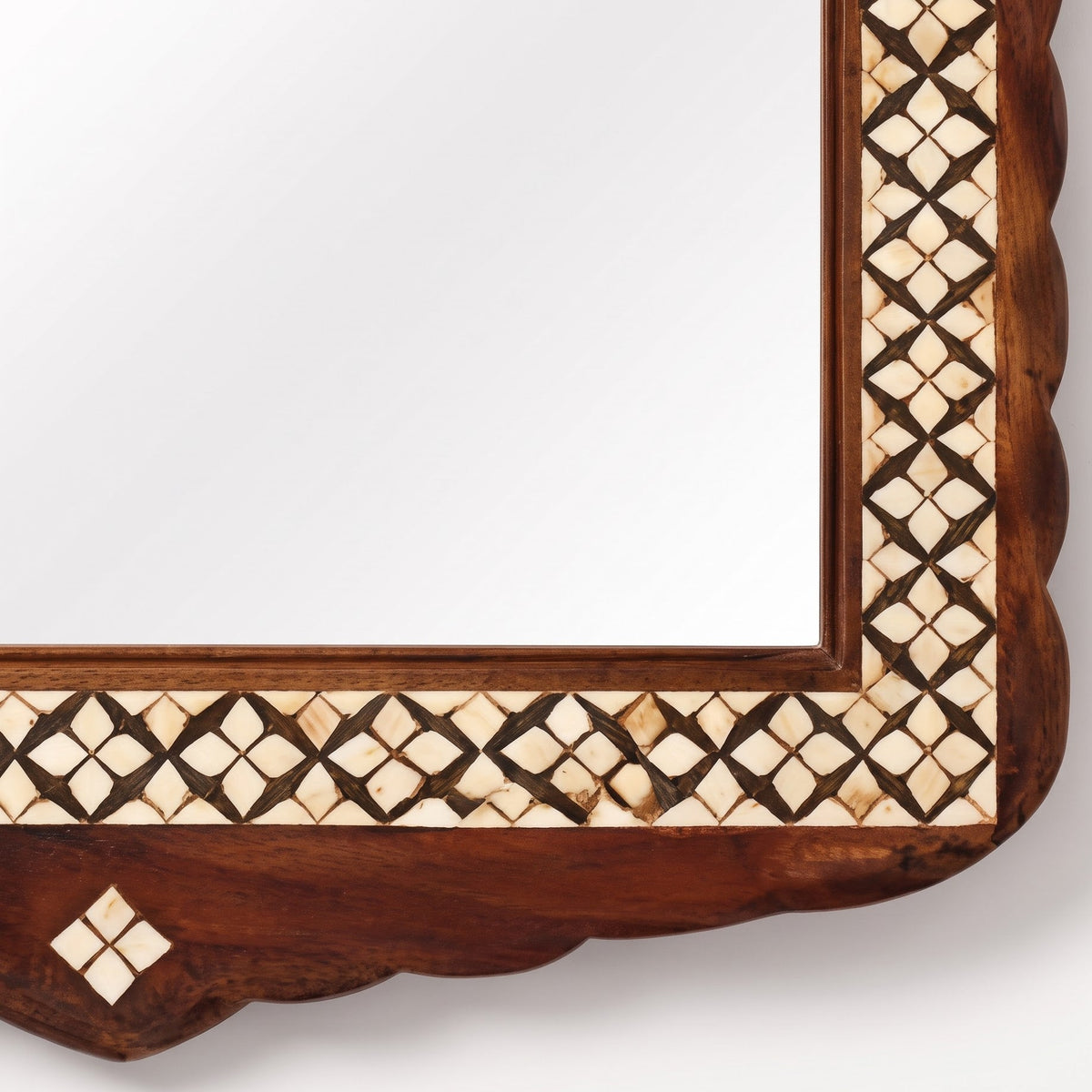 Close-up of a decorative wooden mirror frame with a scalloped edge and an inlaid geometric pattern in dark brown and cream tones.