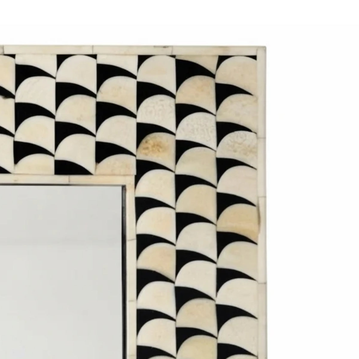Close-up of a decorative rectangular mirror frame with a black and ivory geometric shell-like pattern, showing part of the reflective mirror surface on a white background.