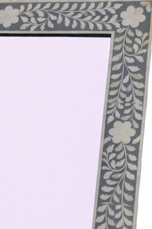 Close-up of a decorative rectangular frame corner with a gray border featuring an off-white floral and leaf inlay pattern, set against a pale lavender background.