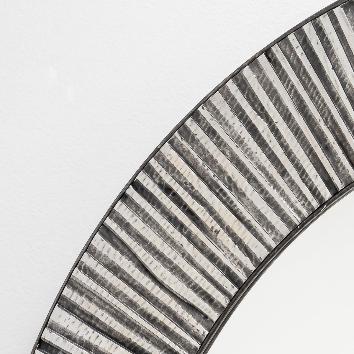 Close-up of a round wall mirror with a textured, ribbed metallic frame in silver and black tones against a plain white background.
