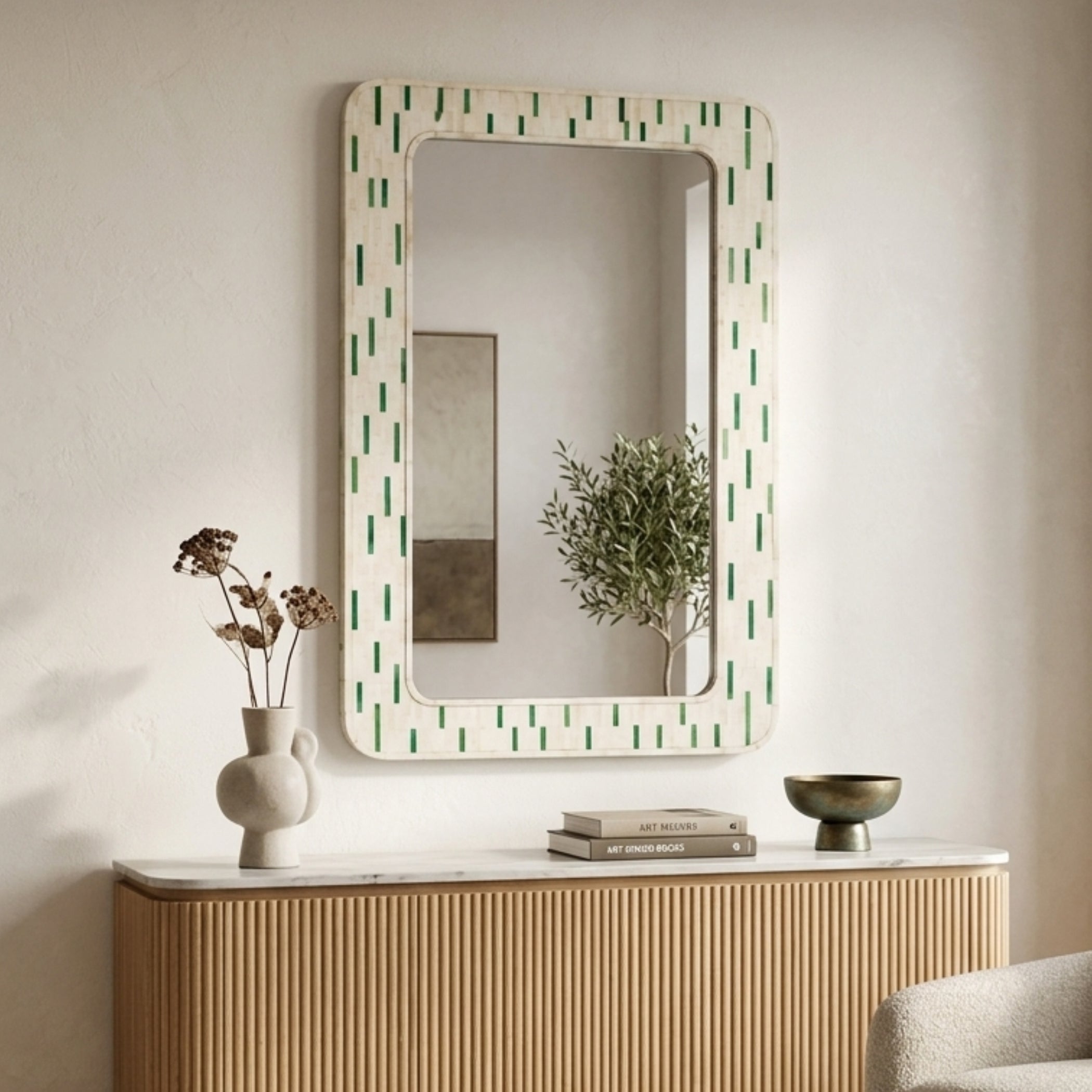 A rectangular wall mirror with a cream-colored frame featuring a green vertical dash pattern, styled on a light wood console table against a textured beige wall.