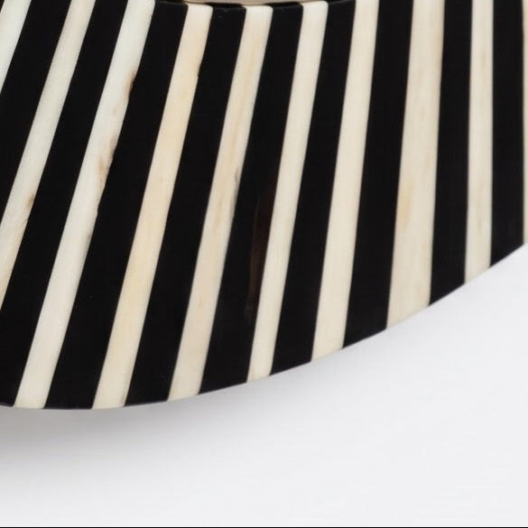 A close-up of a decorative wall mirror with a curved frame featuring alternating black and off-white bone inlay stripes, set against a plain white background.