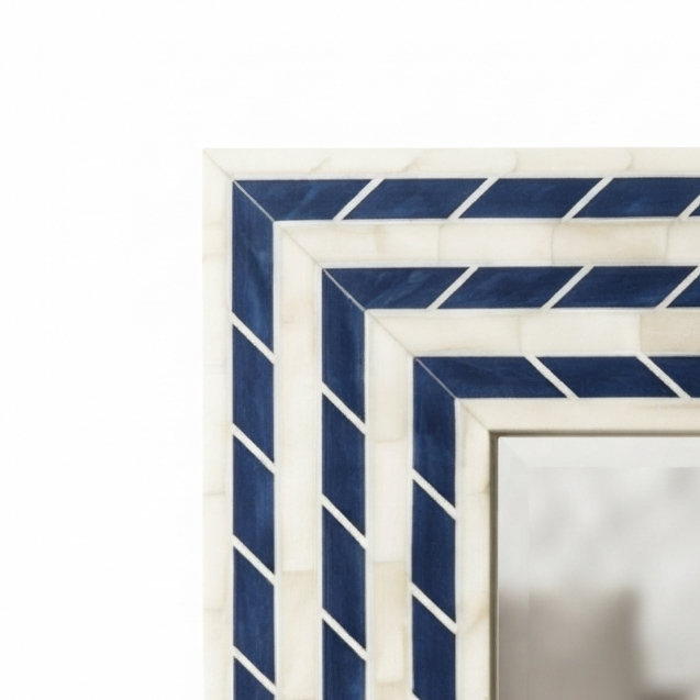 Close-up of a decorative rectangular mirror frame with layered geometric borders in navy blue and off-white, showing a softly blurred interior scene reflected in the glass.