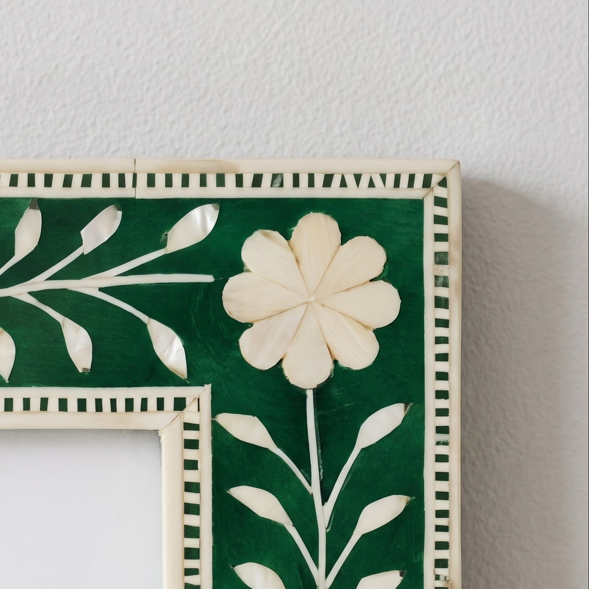 Close-up of a decorative picture frame corner with a dark green background and cream-colored mother-of-pearl floral inlay.