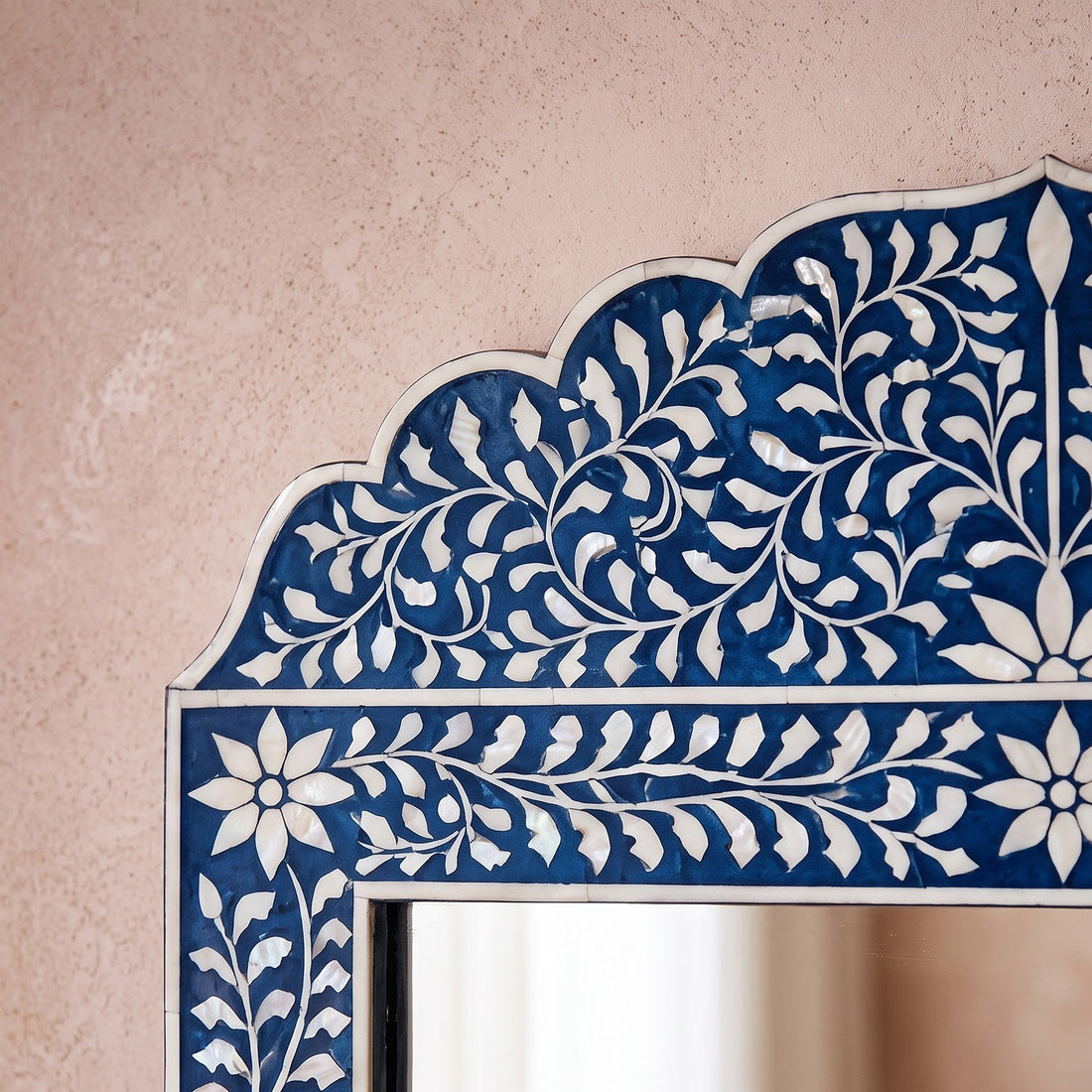 Decorative mirror with floral frame on a wall above a console table with flowers and candles.