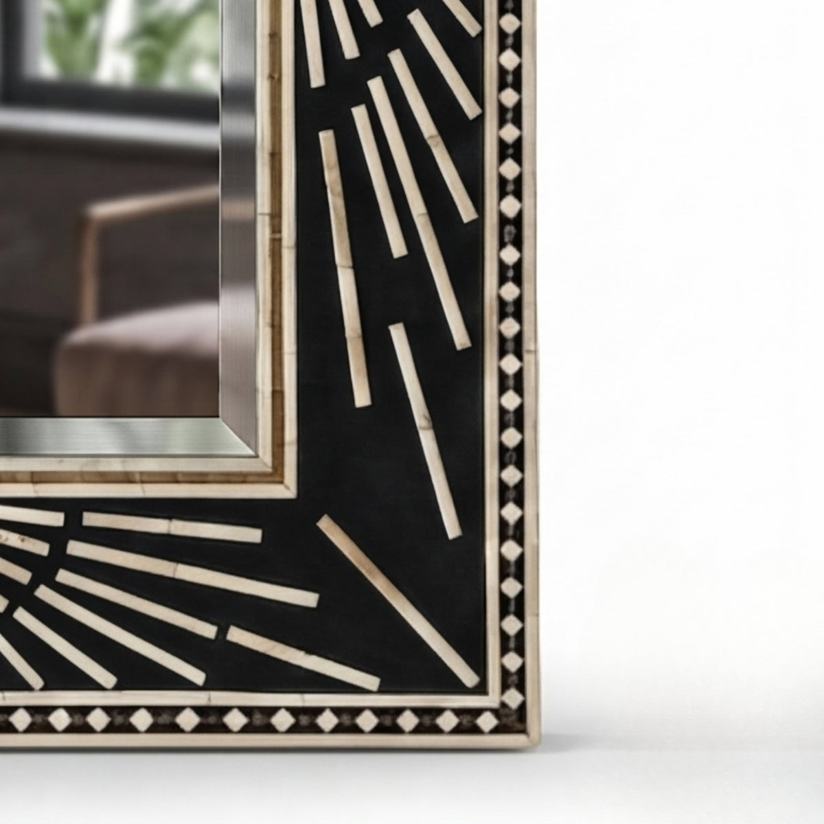 Close-up corner of a decorative rectangular mirror with a black inlay featuring cream-colored geometric bone or mother-of-pearl patterns and a light wood frame.