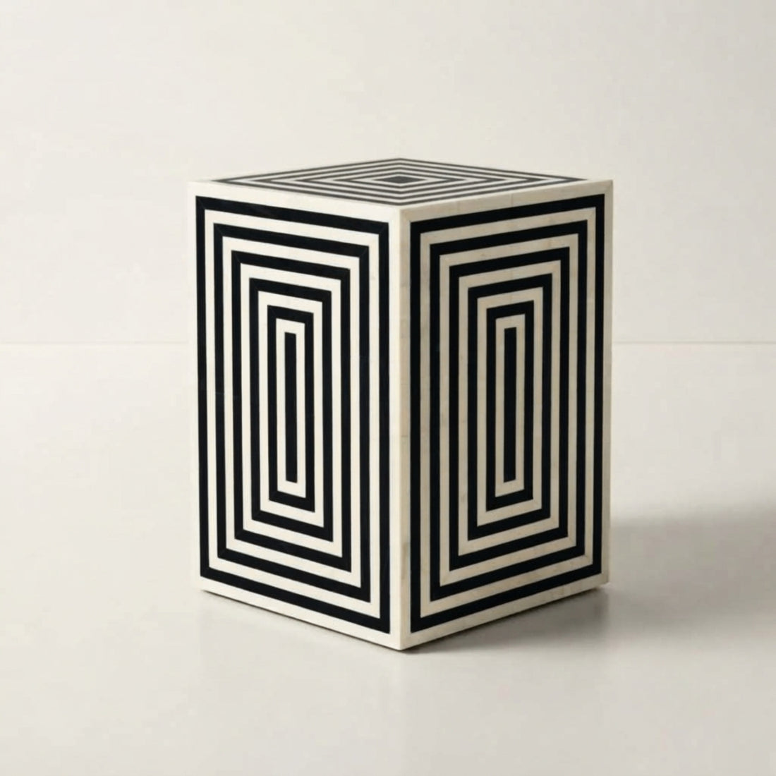 A modern side table with a bold black and white geometric concentric square pattern on its cube-shaped side, styled in a contemporary living room next to a cream bouclé sofa.