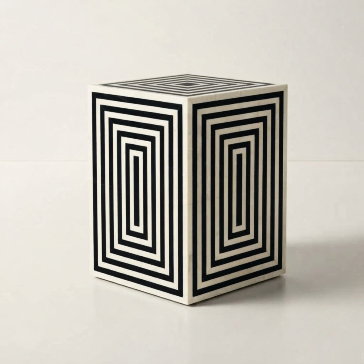 A cube-shaped decorative side table or stool with a black and white geometric concentric rectangle pattern, shown on a clean white studio background.