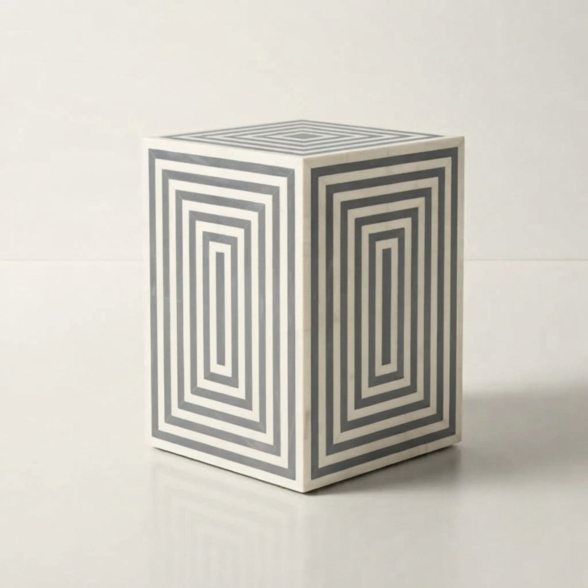 A cube-shaped side table with a white base and gray concentric geometric stripe patterns on two visible sides, photographed on a clean white studio background.