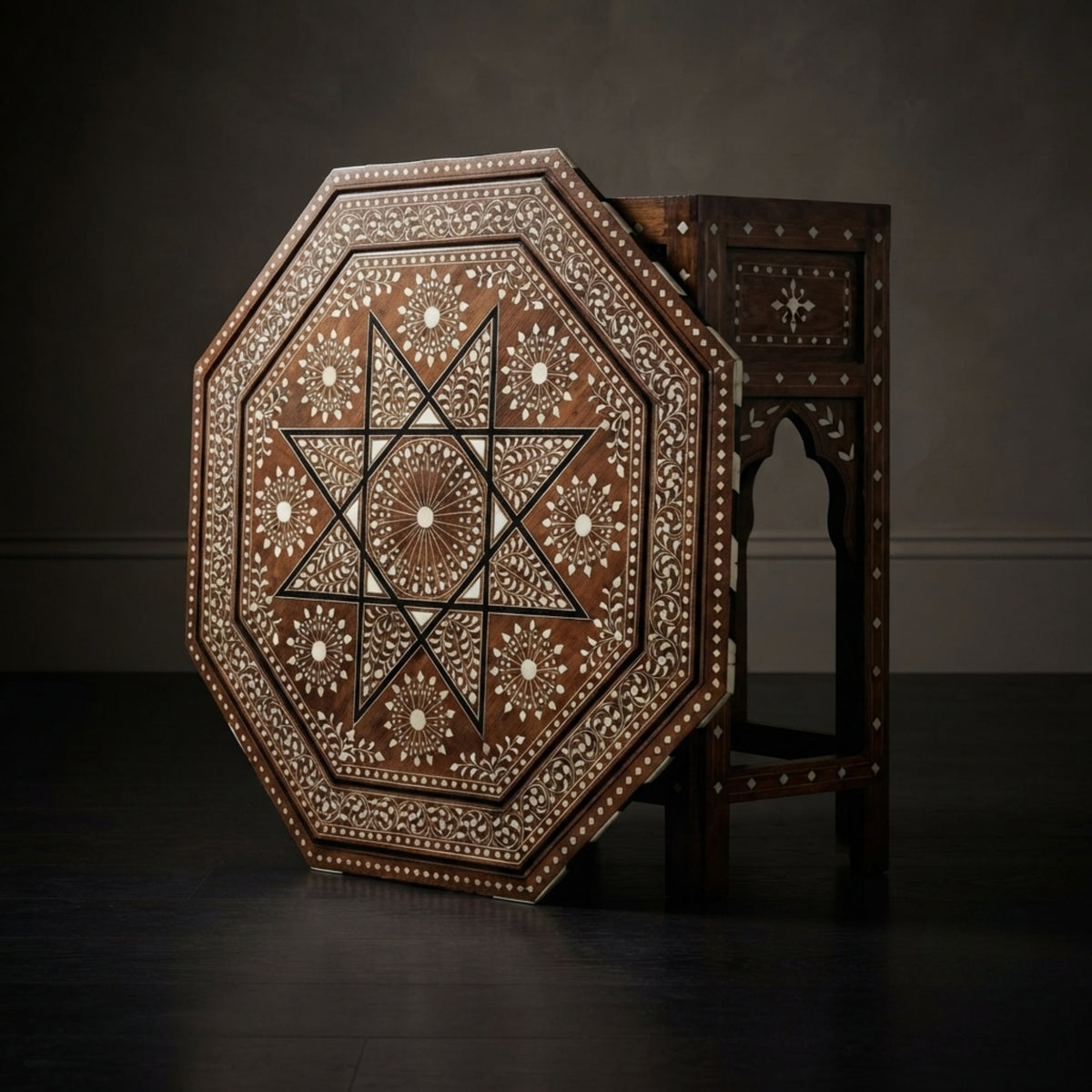 An octagonal wooden table with intricate bone or mother-of-pearl inlay patterns, shown standing open to reveal its dark interior, set against a dark studio background.