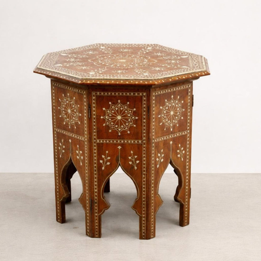 An octagonal wooden end table with intricate bohemian-style inlay patterns, styled in a cozy living room next to a white armchair and a potted fiddle-leaf fig plant.