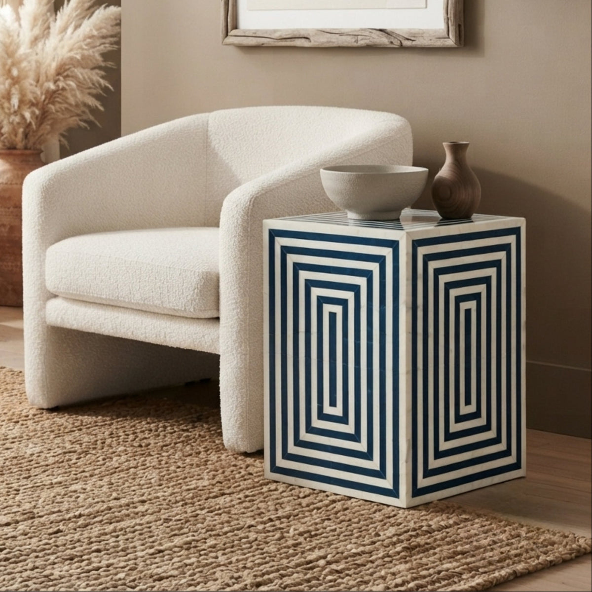 A cream bouclé accent chair in a styled living room next to a white side table with navy blue geometric stripes, decorated with a bowl and vase.