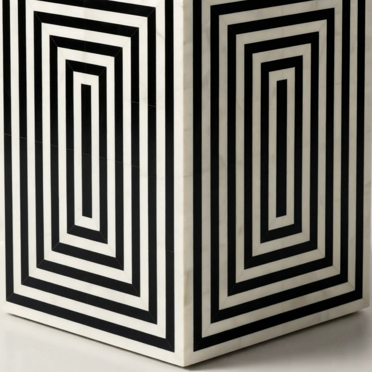 A close-up of a geometric side table or stool featuring a bold black and white concentric rectangular pattern on a light stone or marble-like surface.