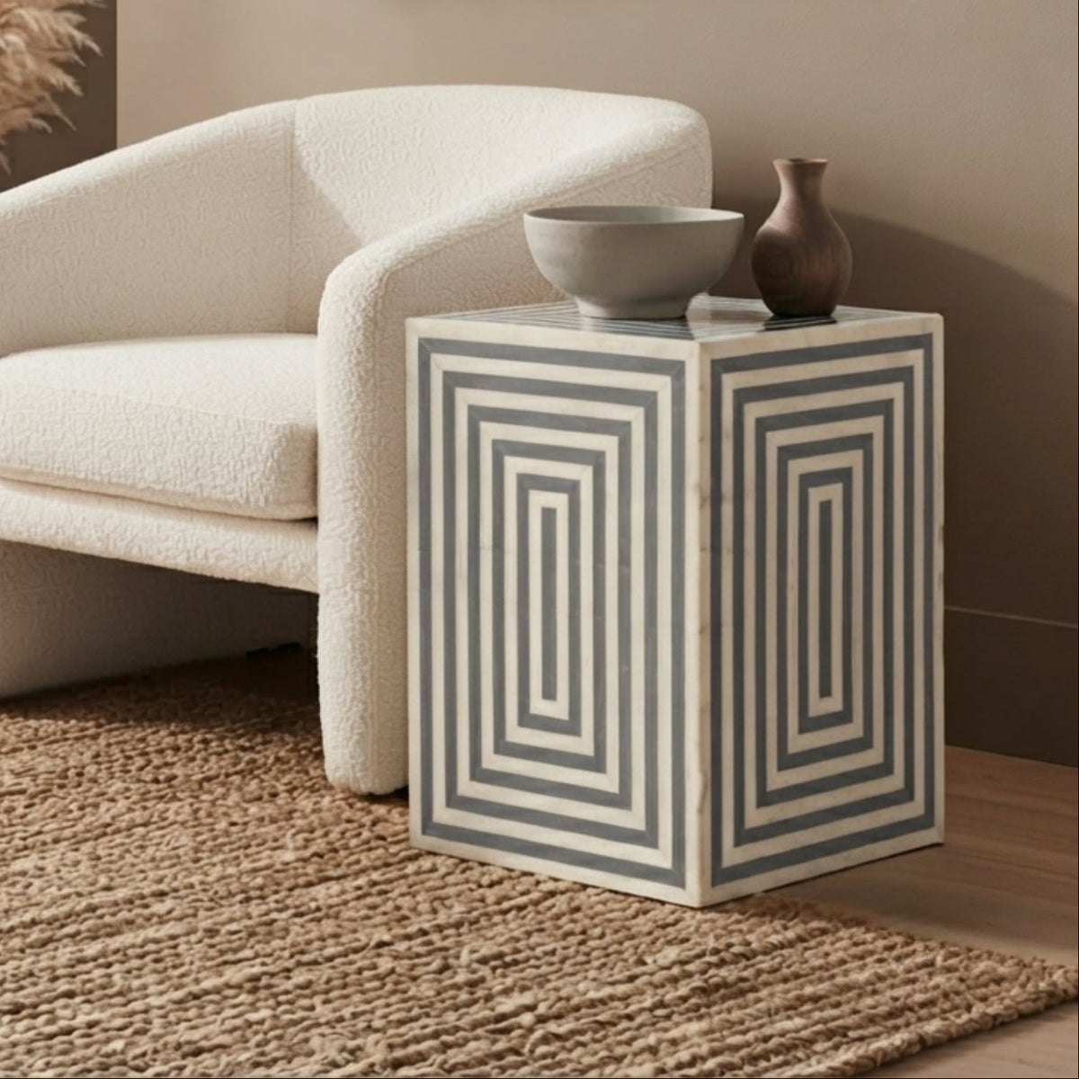 A cream bouclé armchair in a styled living room setting next to a geometric side table, with a woven rug, pampas grass, and neutral decor.